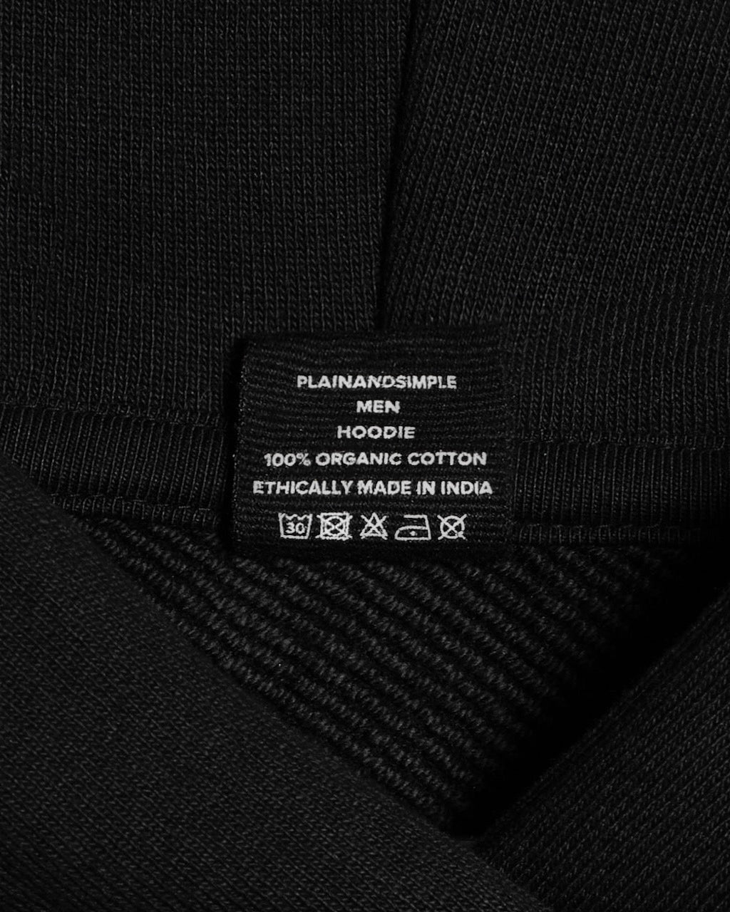 A close up of an neck label in a men's black oversized heavyweight organic cotton hoodie.