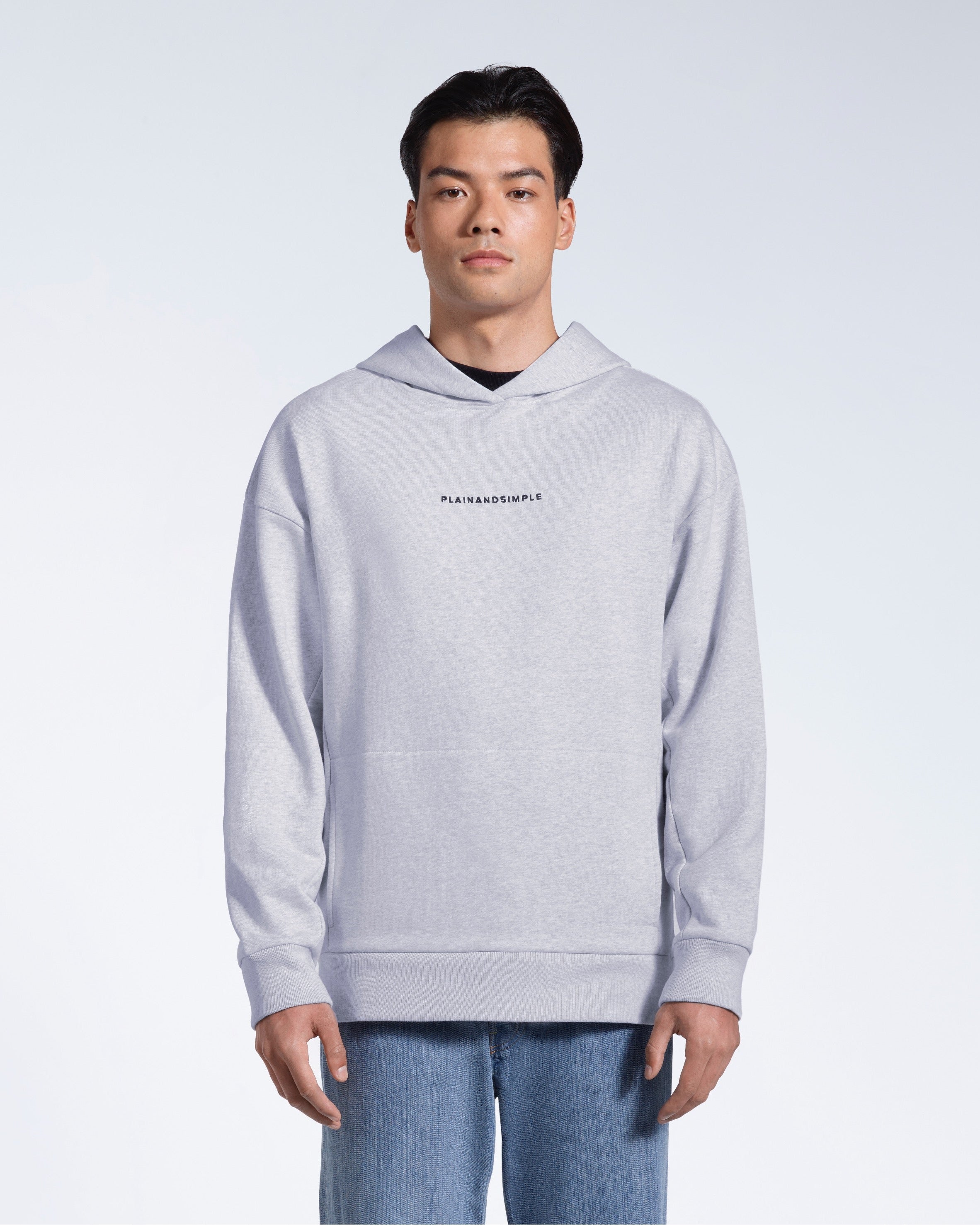 A man facing front on looking into the camera with his arms by his sides, modelling a branded grey oversized heavyweight organic cotton hoodie.