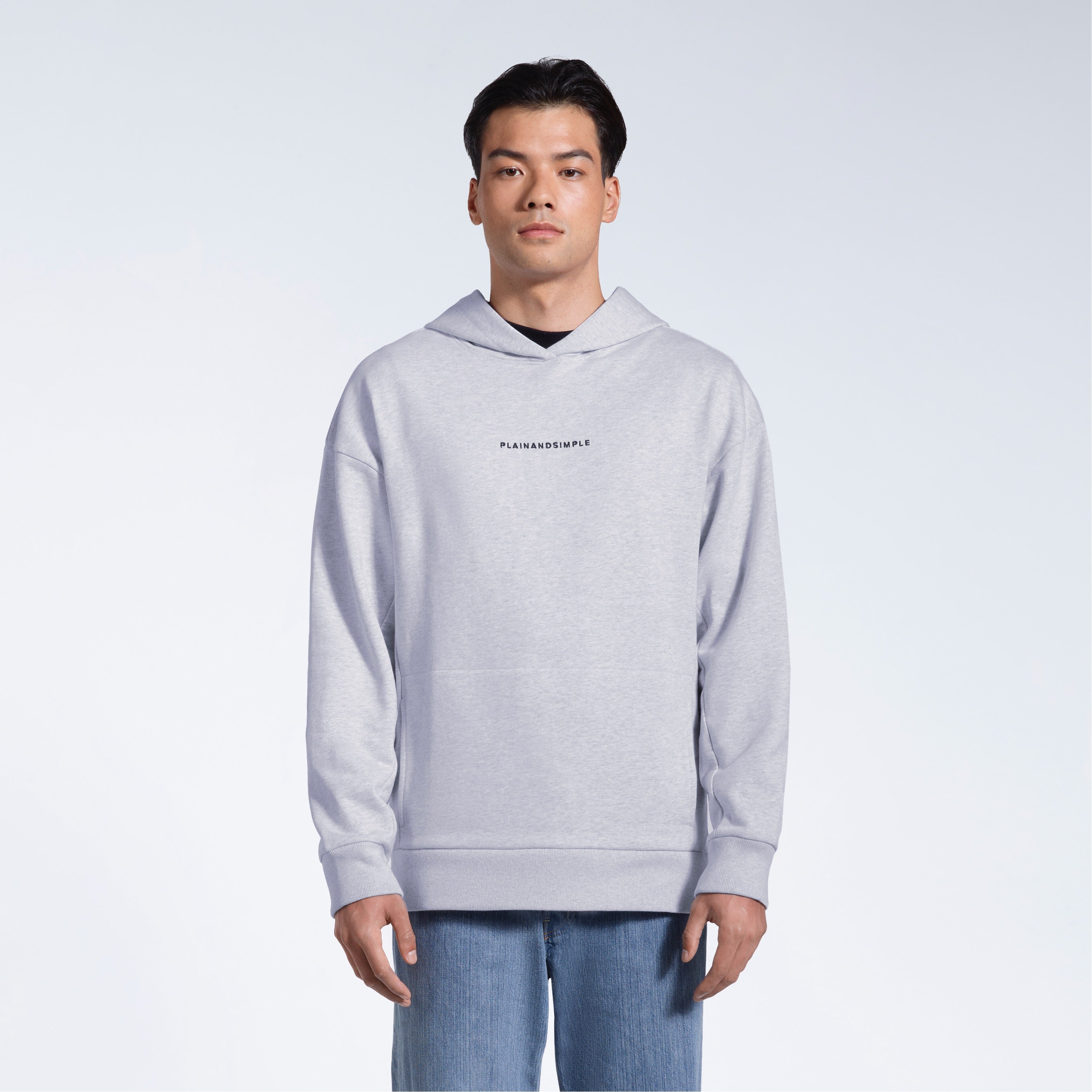 A man facing front on looking into the camera with his arms by his sides, modelling a branded grey oversized heavyweight organic cotton hoodie.