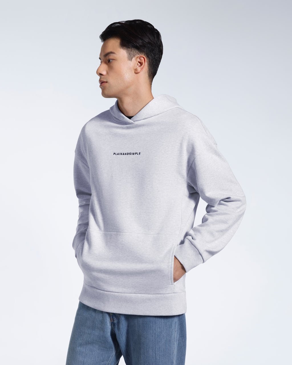 A man looking away from the camera with his hands in his pockets, modelling a branded grey oversized heavyweight organic cotton hoodie.