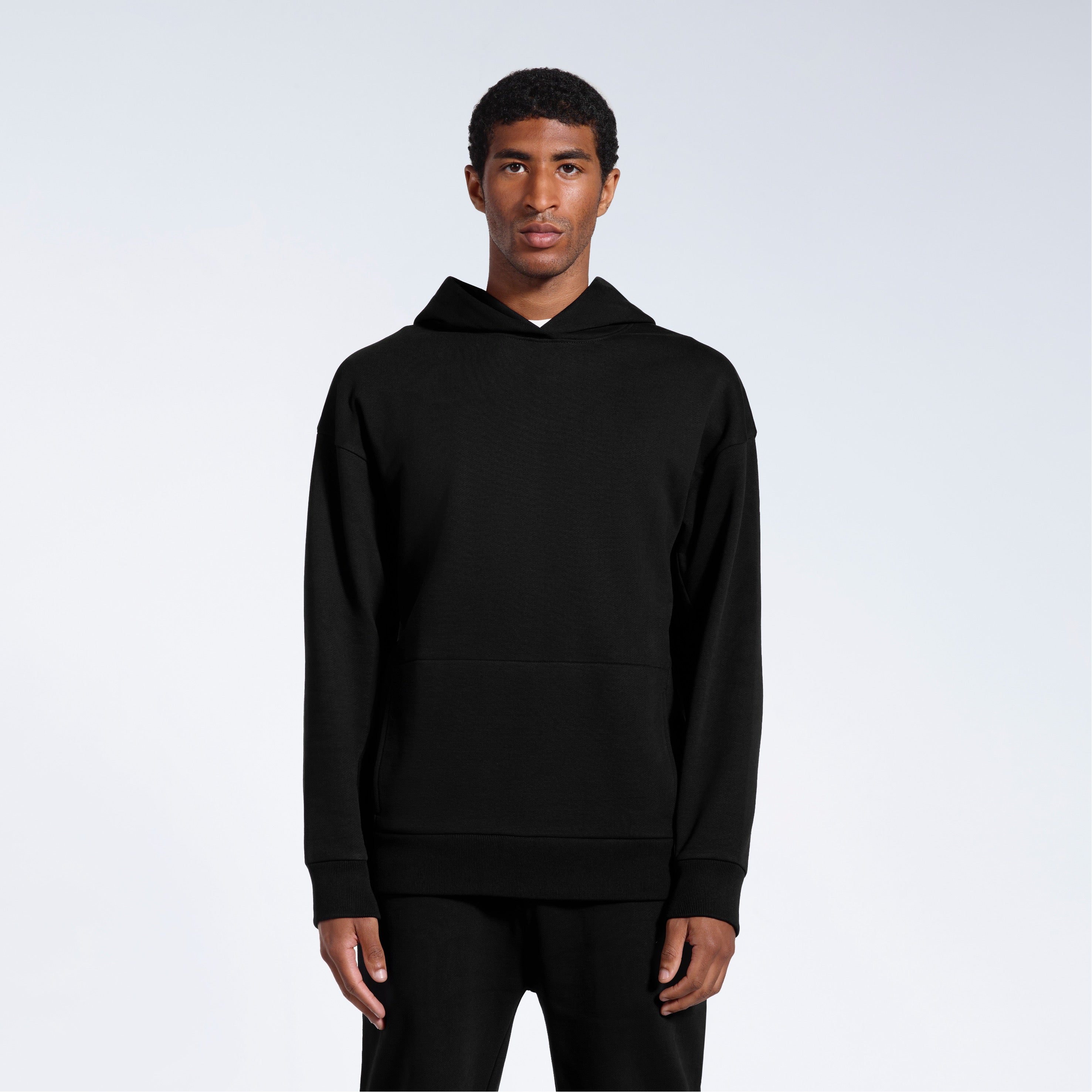 A man facing front on looking into the camera with his arms by his sides, modelling a black oversized heavyweight organic cotton hoodie.
