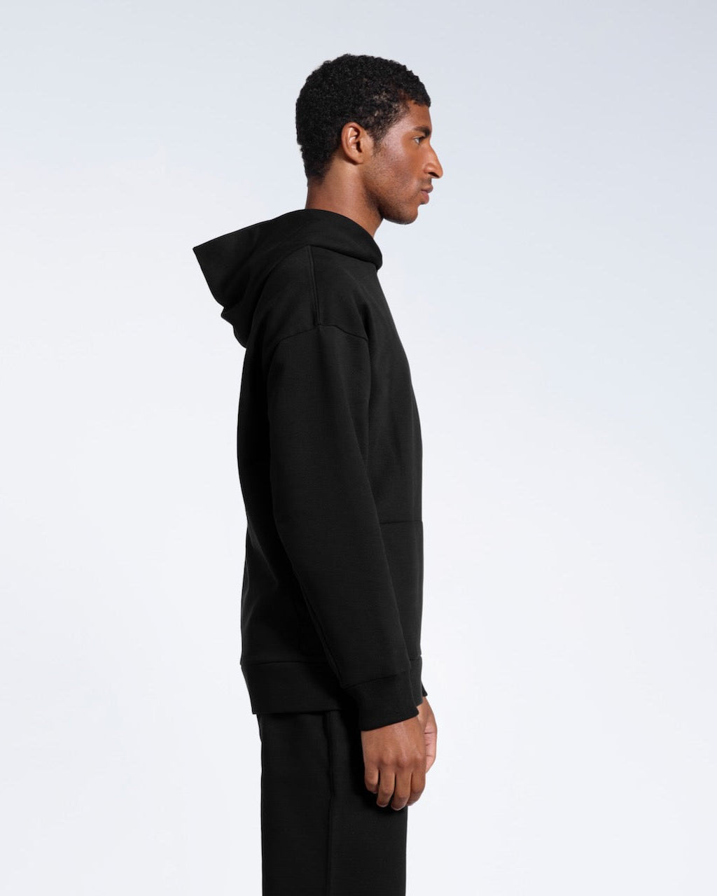 A man facing side on, modelling a black oversized heavyweight organic cotton hoodie.