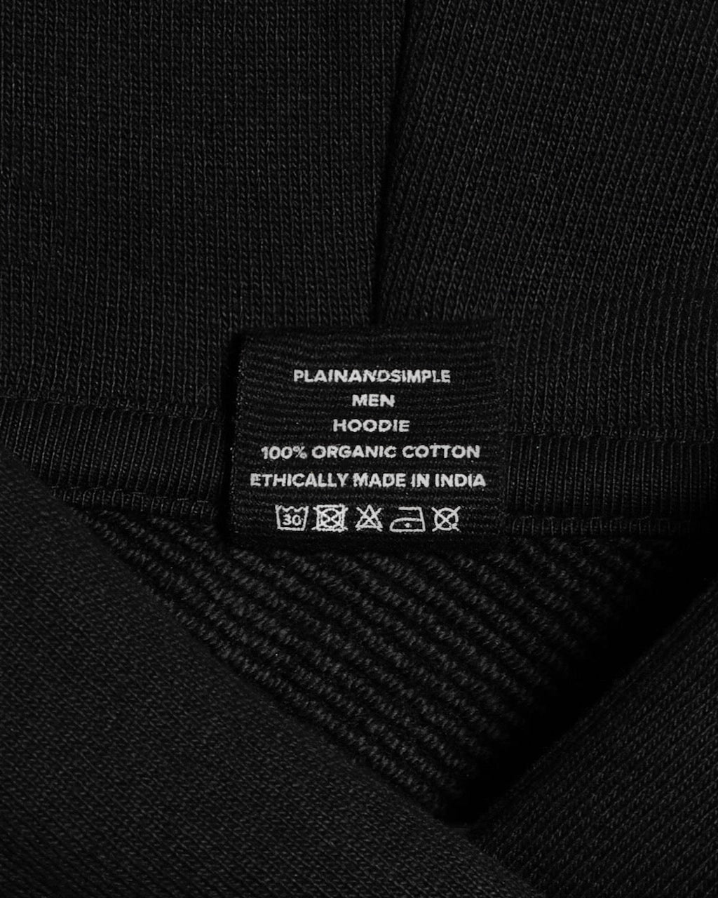 A close up of an neck label in a men's black oversized heavyweight organic cotton hoodie.