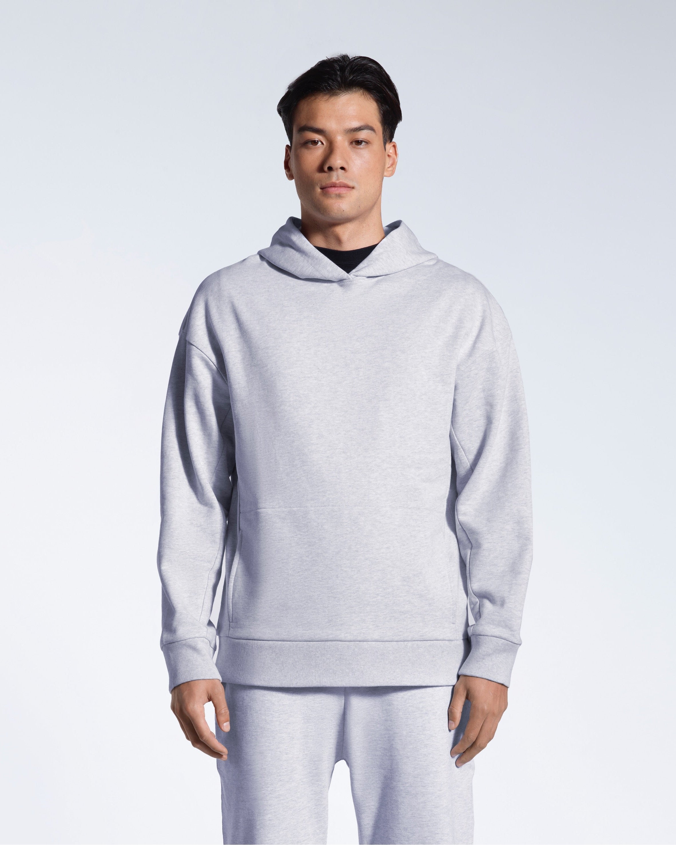 A man looking into the camera with his arms by his sides, modelling a grey oversized heavyweight organic cotton hoodie with matching joggers.