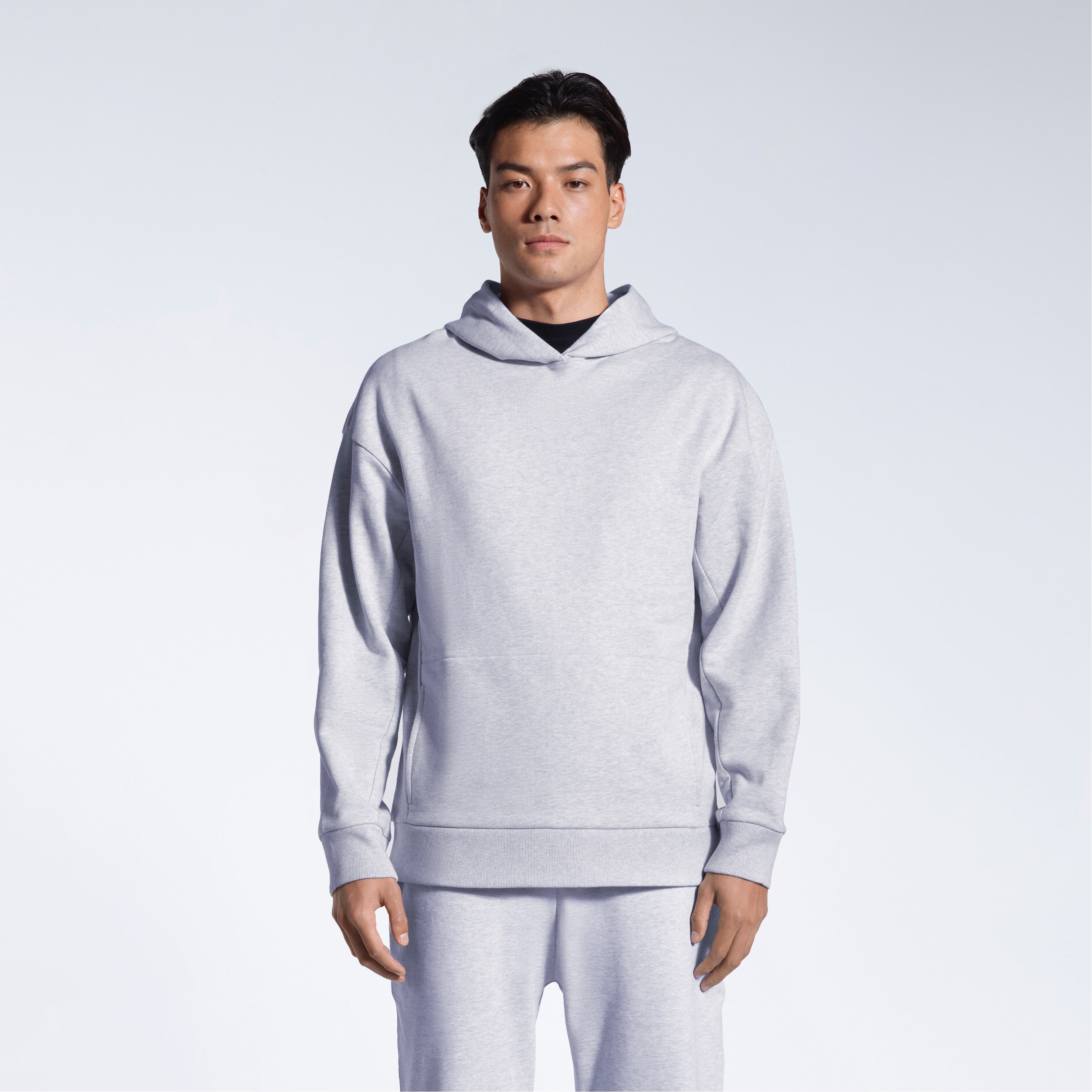 A man looking into the camera with his arms by his sides, modelling a grey oversized heavyweight organic cotton hoodie with matching joggers.