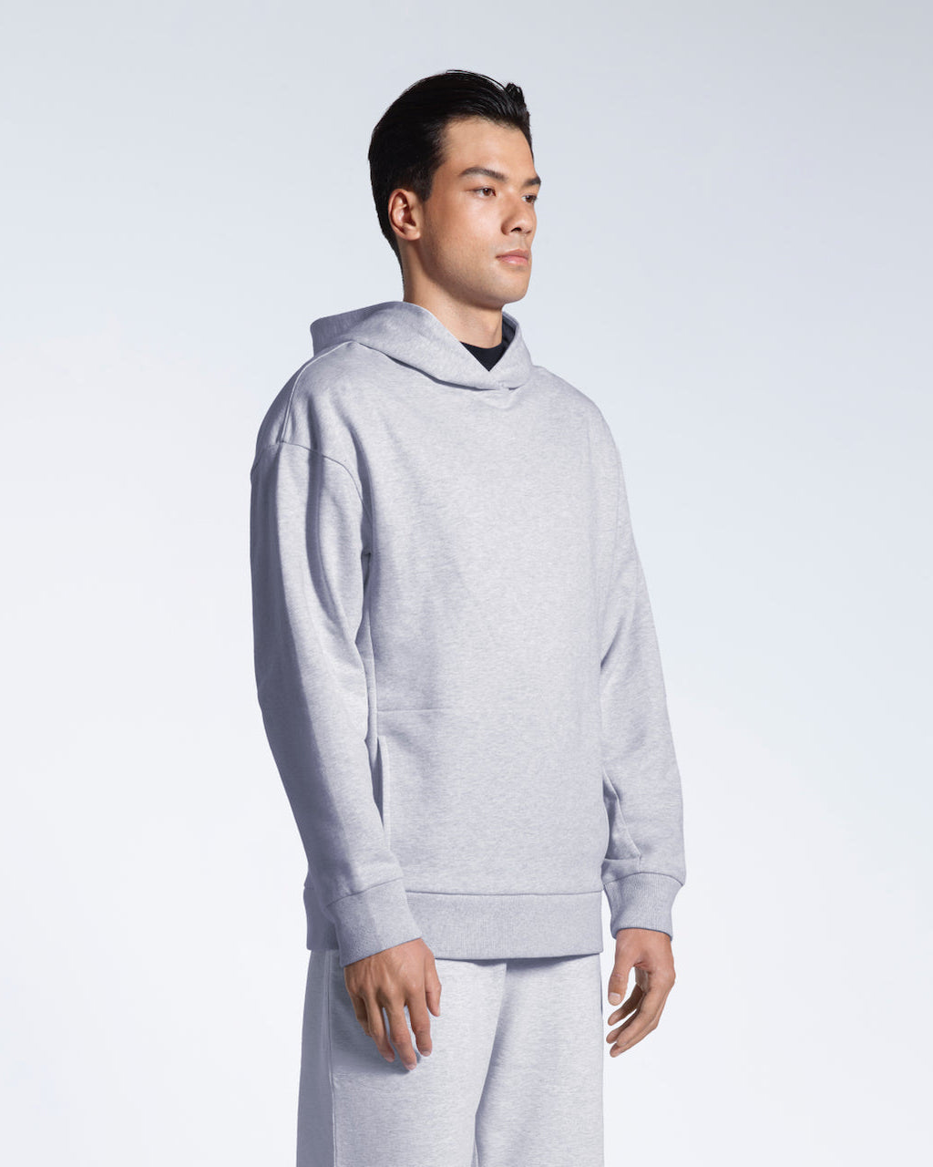 A man looking away from the camera with his arms by his side, modelling a grey oversized heavyweight organic cotton hoodie with matching joggers.