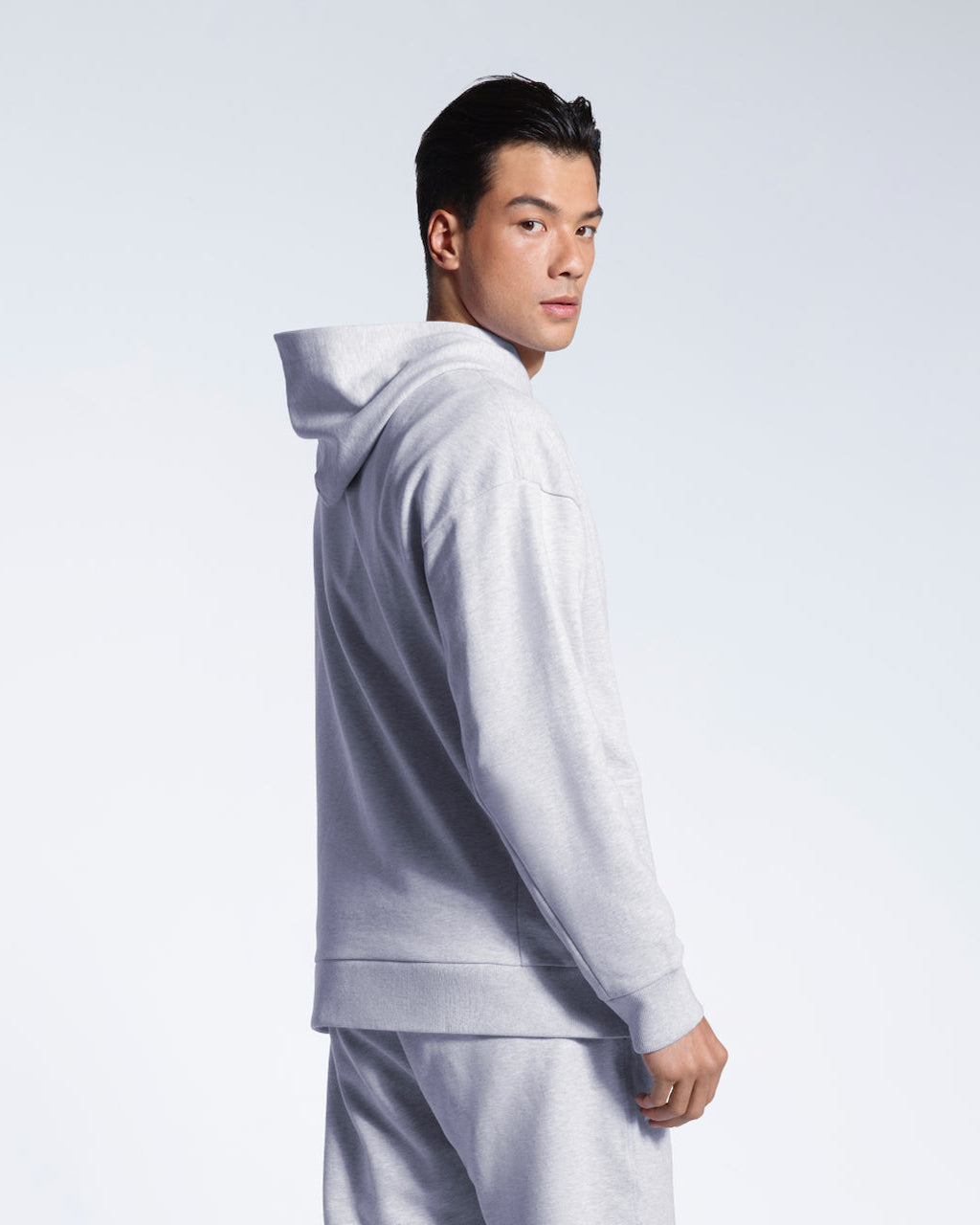 A man with his head turned towards the camera, showing the back of his grey oversized heavyweight organic cotton hoodie with matching joggers.