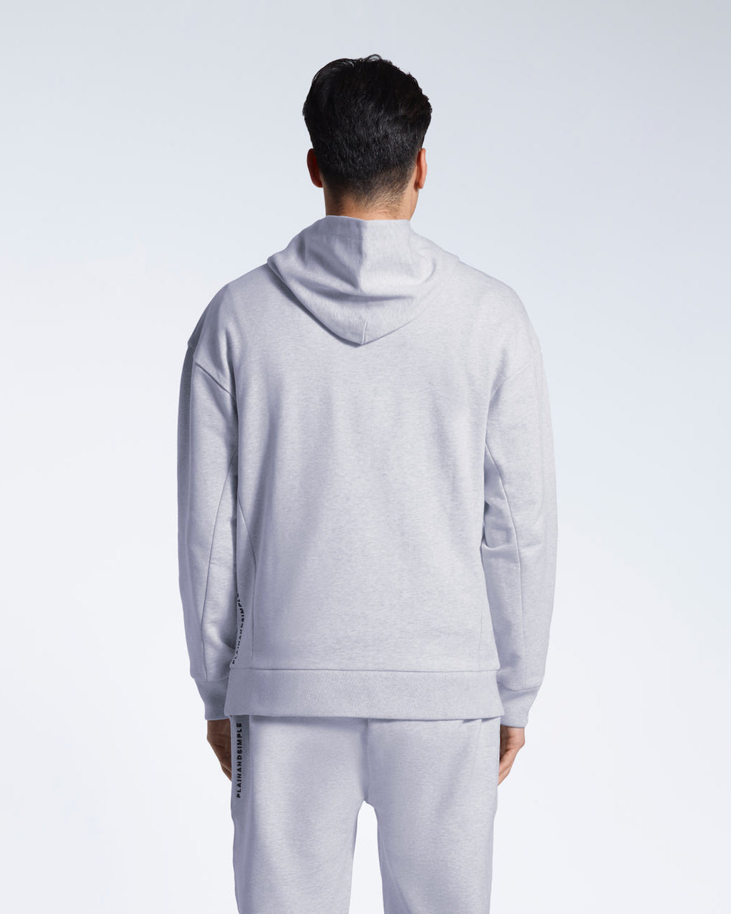 A man facing away from the camera with his arms by his sides, modelling a grey oversized heavyweight organic cotton hoodie with matching joggers.
