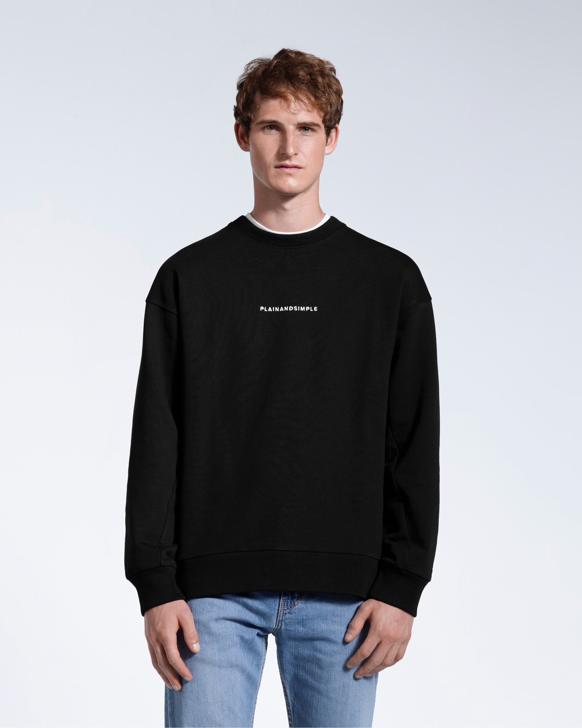 A man face on with his arms by his side, modelling a branded black oversized heavyweight organic cotton sweatshirt.