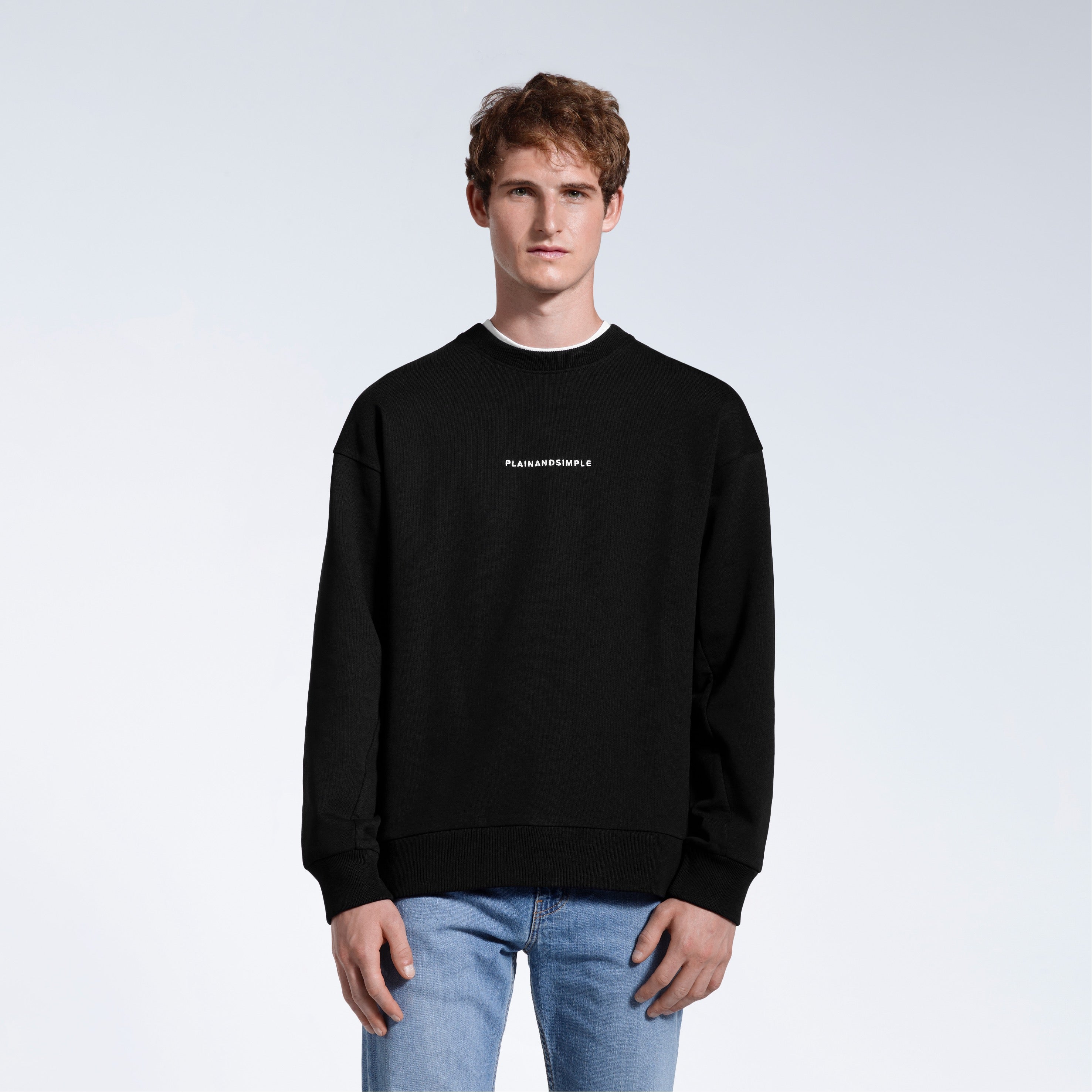 A man face on with his arms by his side, modelling a branded black oversized heavyweight organic cotton sweatshirt.