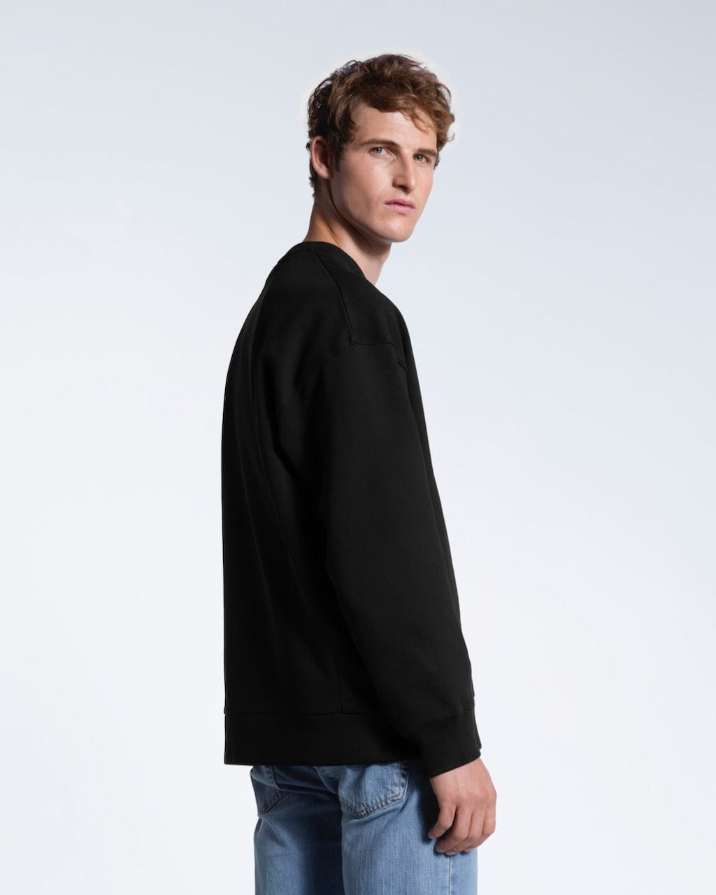 A man turned to look at the camera, showing the back of his black oversized heavyweight organic cotton sweatshirt.