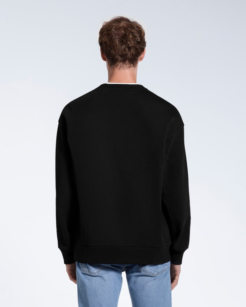 A man facing away from the camera, showing the back of his black oversized heavyweight organic cotton sweatshirt.