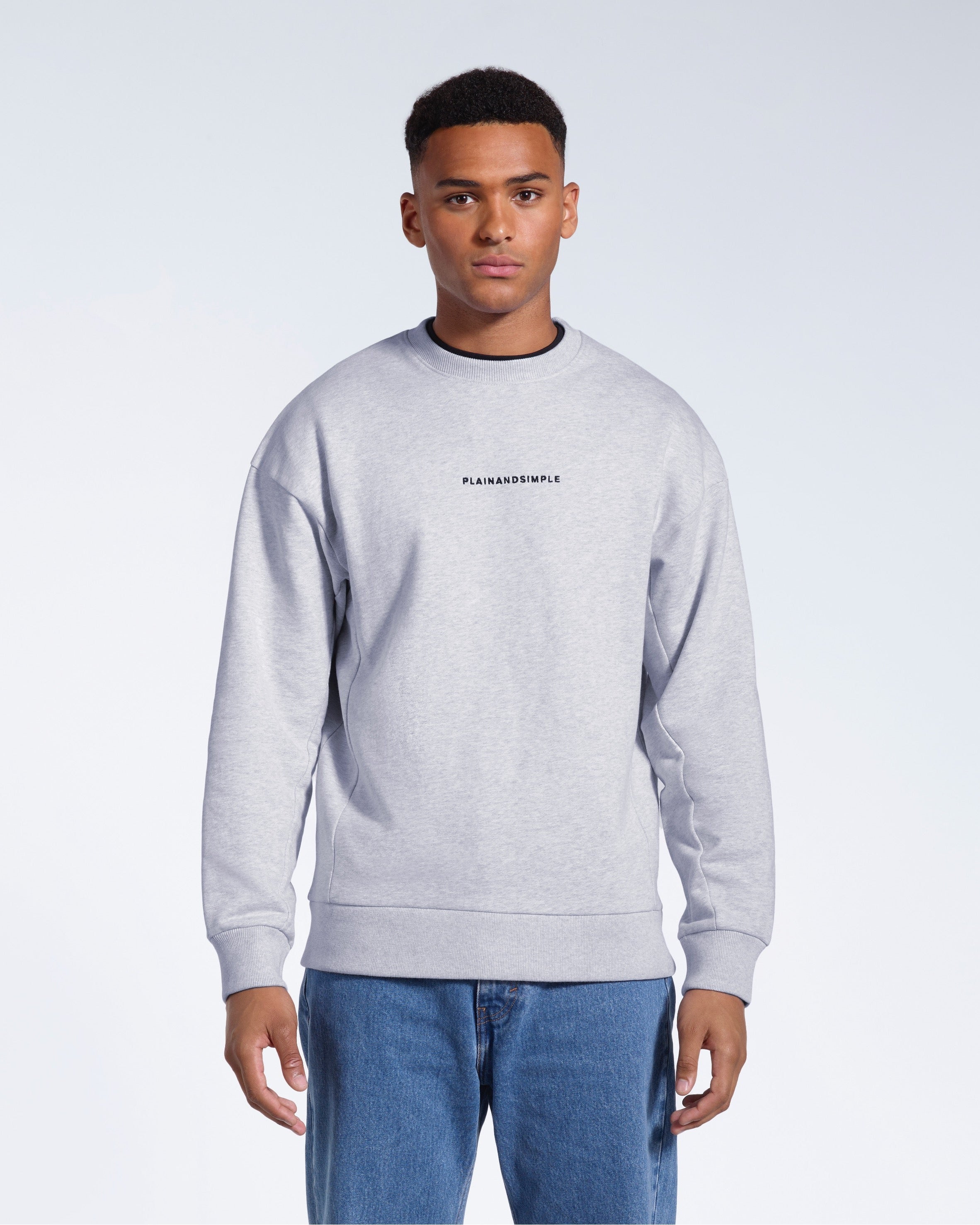 A man face on with his arms by his side, modelling a branded grey oversized heavyweight organic cotton sweatshirt.