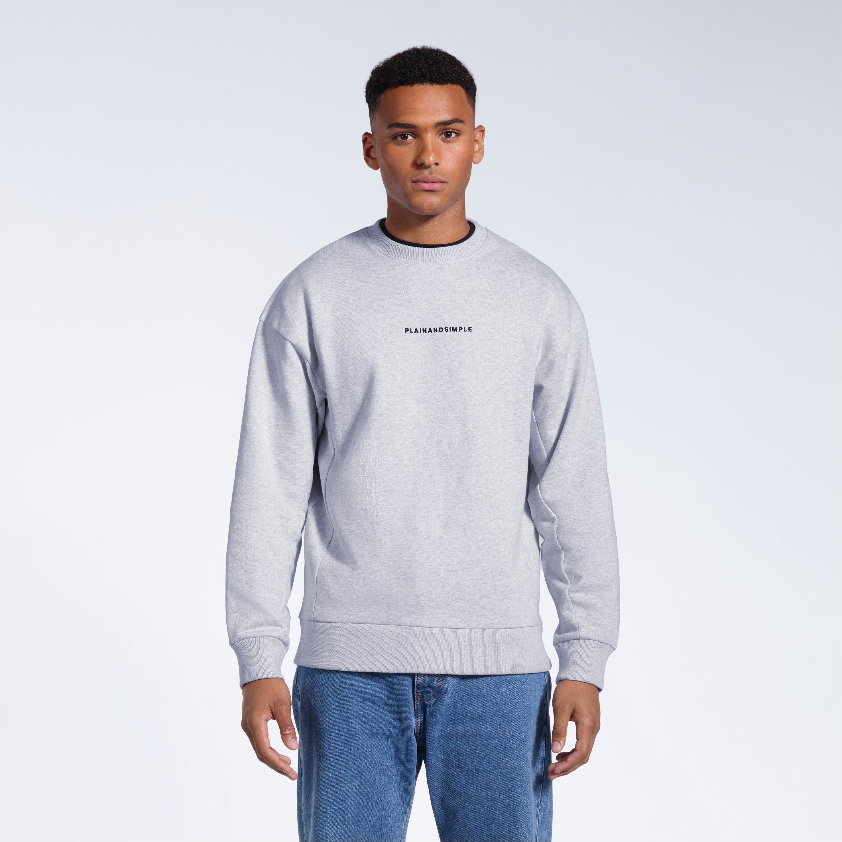 A man face on with his arms by his side, modelling a branded grey oversized heavyweight organic cotton sweatshirt.