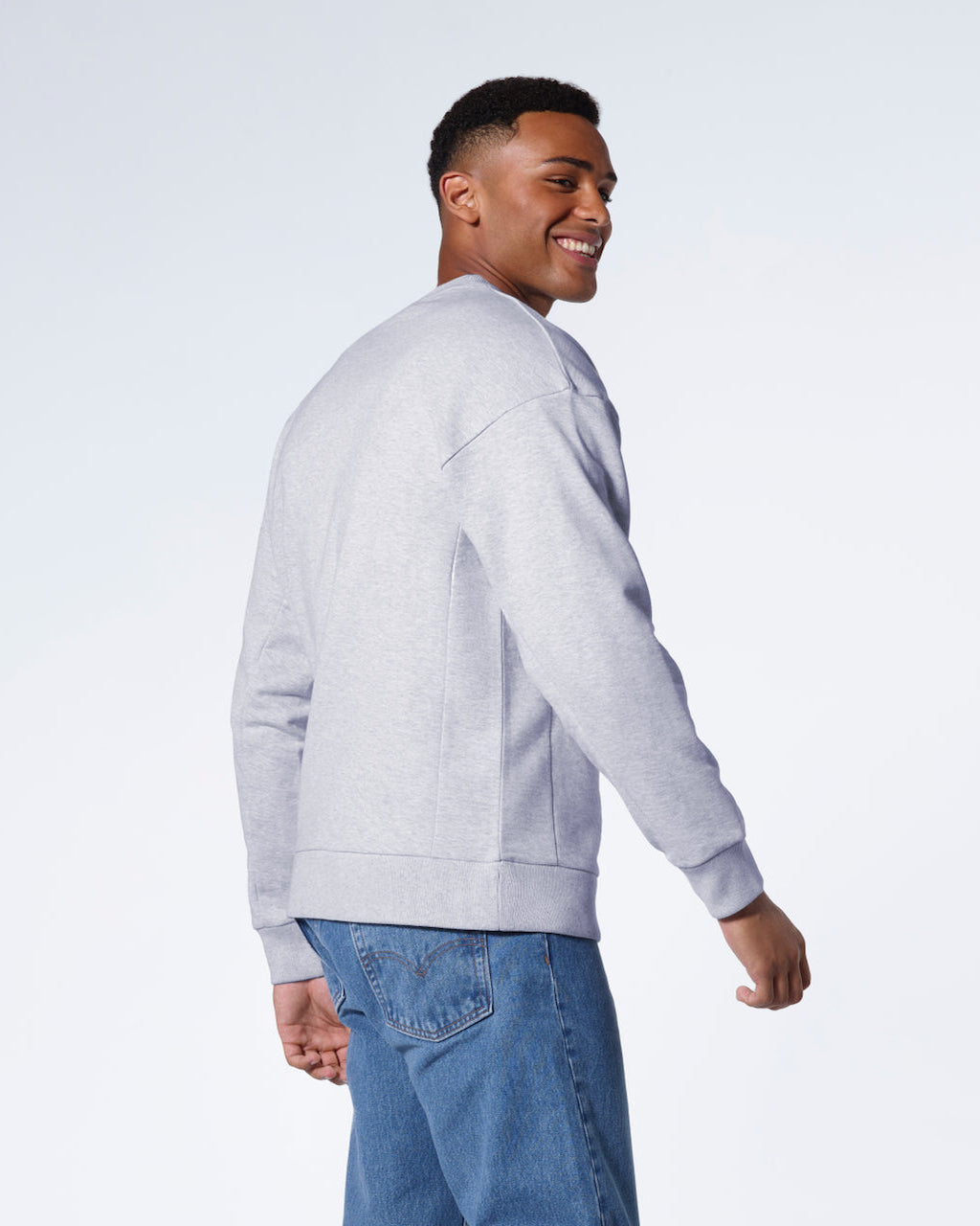 A man smiling, showing the back of his black oversized heavyweight organic cotton sweatshirt.