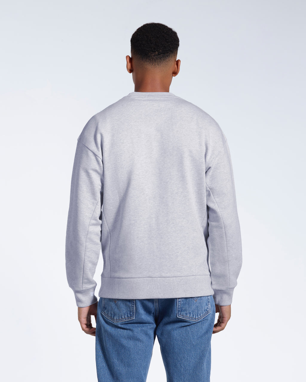 A man facing away from the camera, showing the back of his grey oversized heavyweight organic cotton sweatshirt.