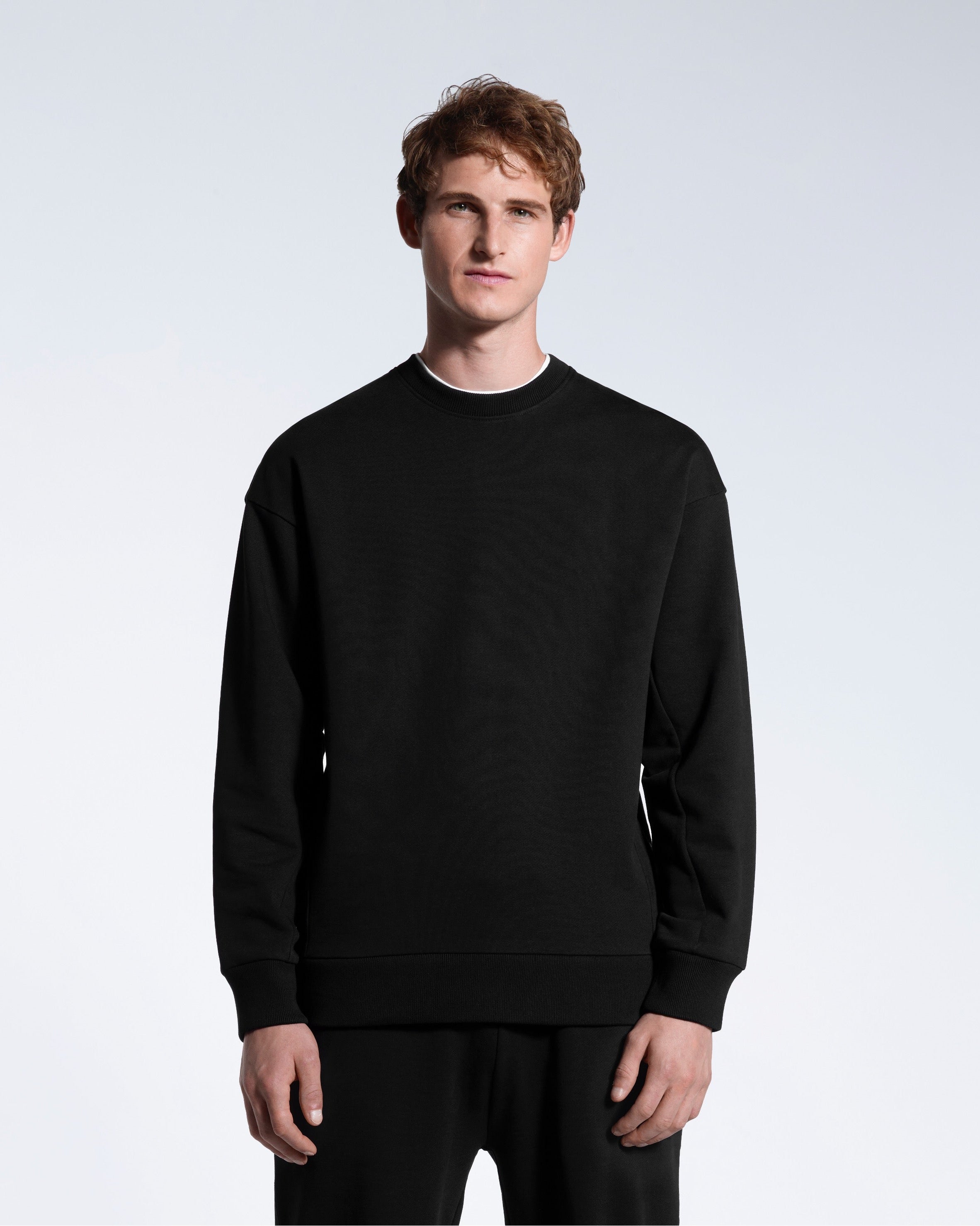 A man face on with his arms by his side, modelling a black oversized heavyweight organic cotton sweatshirt with matching joggers.