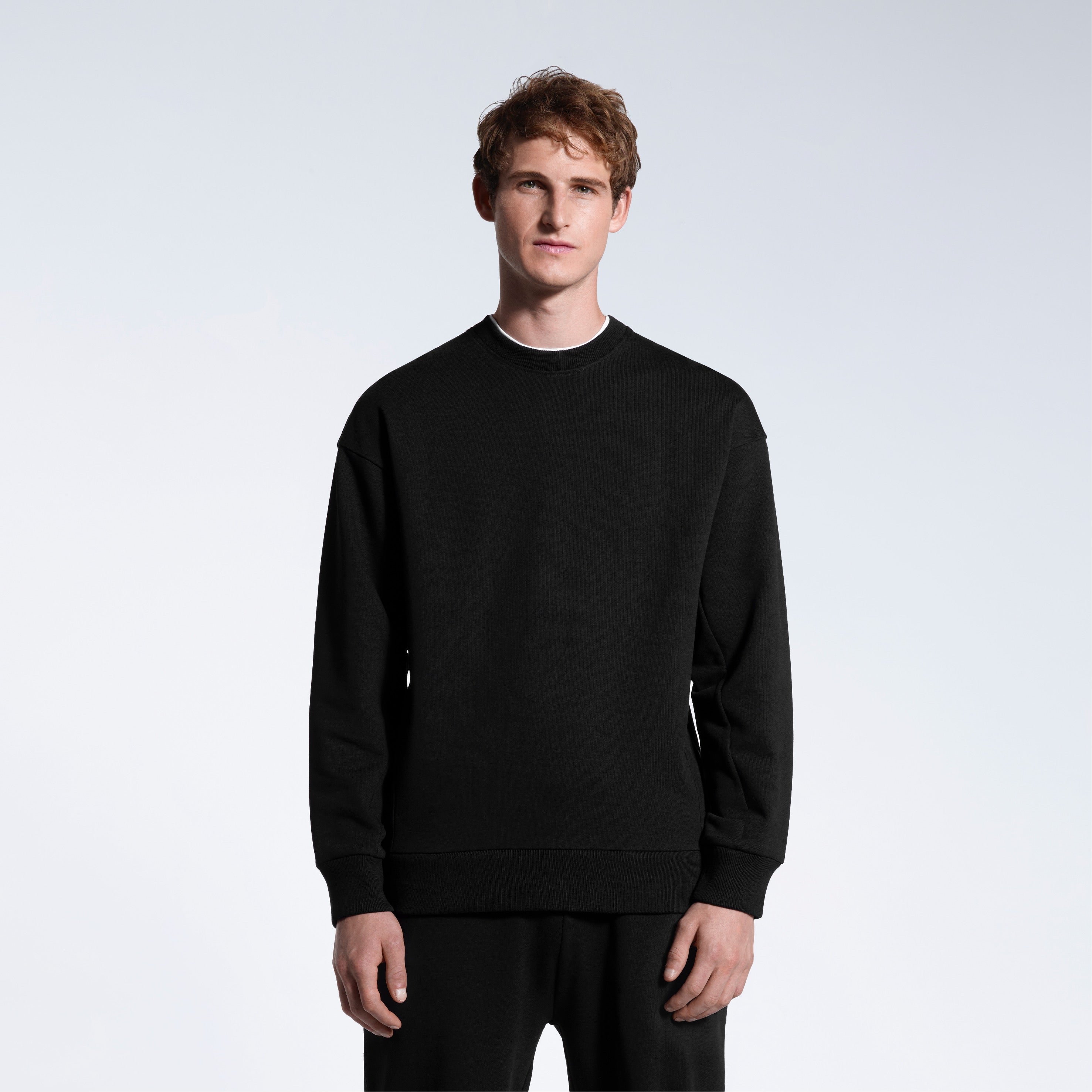 A man face on with his arms by his side, modelling a black oversized heavyweight organic cotton sweatshirt with matching joggers.
