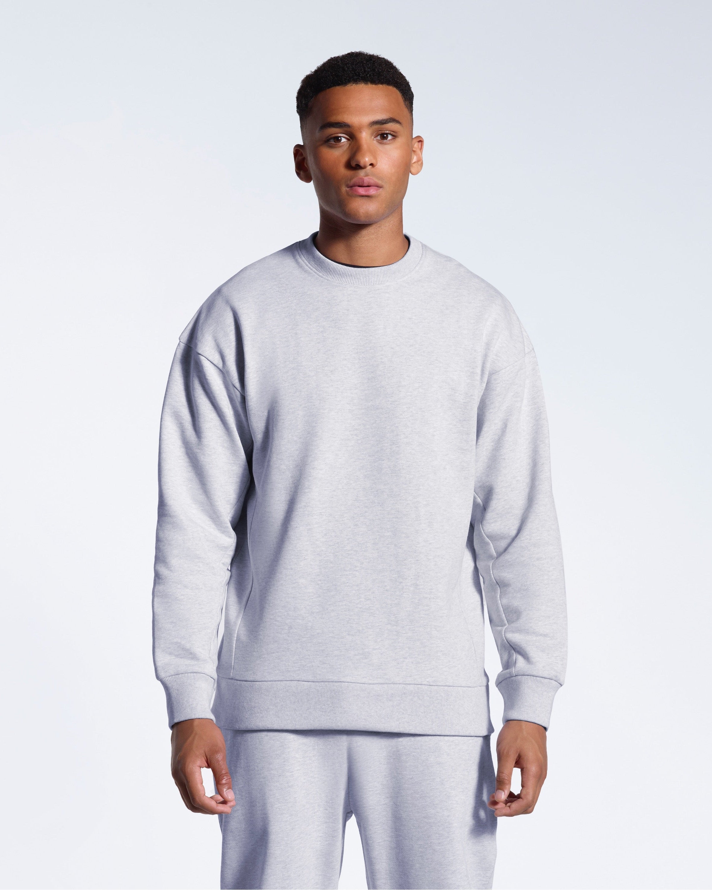 A man face on with his arms by his side, modelling a plain grey oversized heavyweight organic cotton sweatshirt with matching joggers.