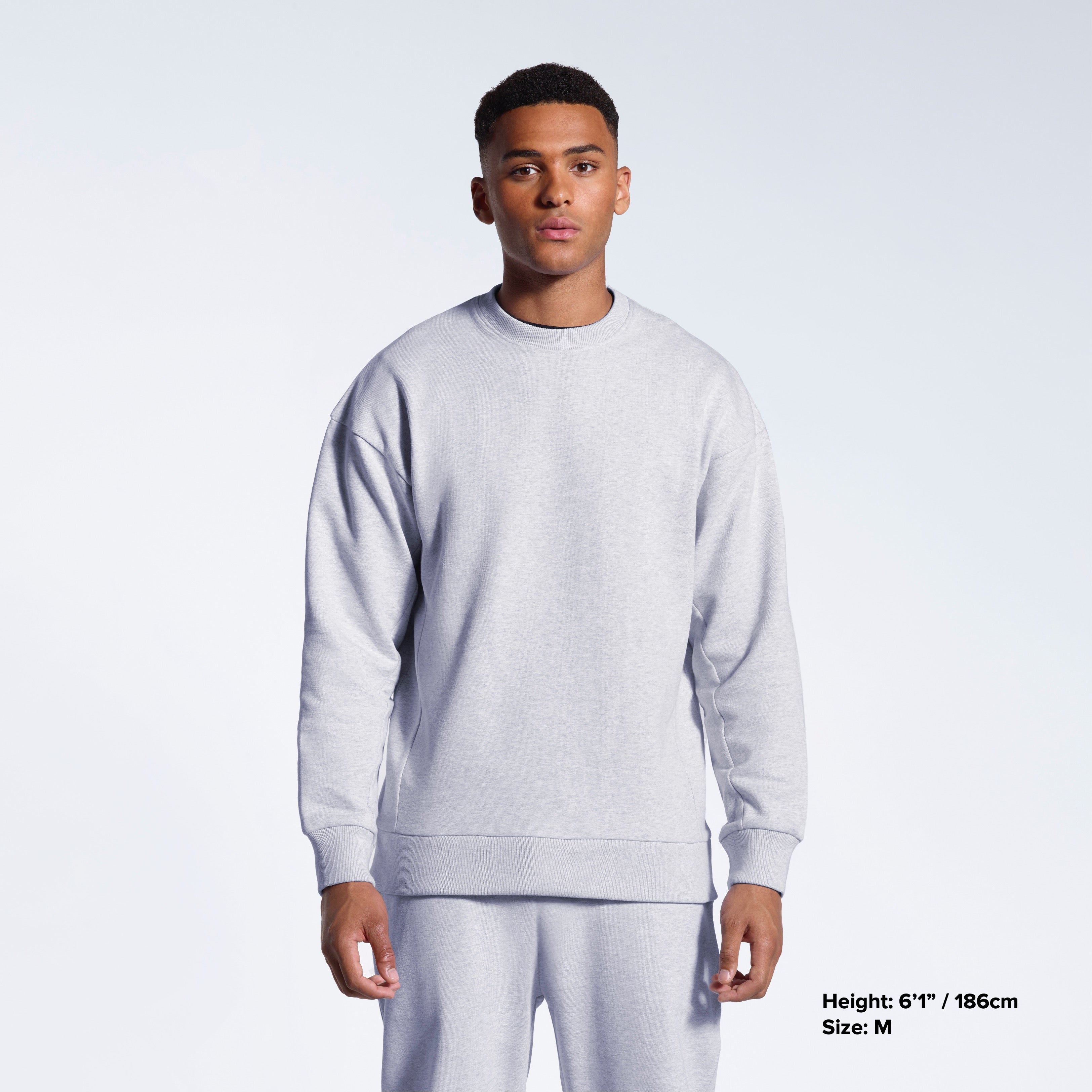 A man face on with his arms by his side, modelling a plain grey oversized heavyweight organic cotton sweatshirt with matching joggers.