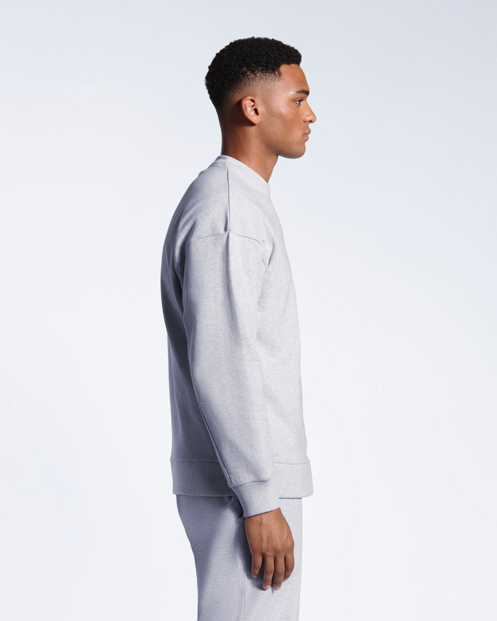A man facing side on, modelling a grey oversized heavyweight organic cotton sweatshirt with matching joggers.