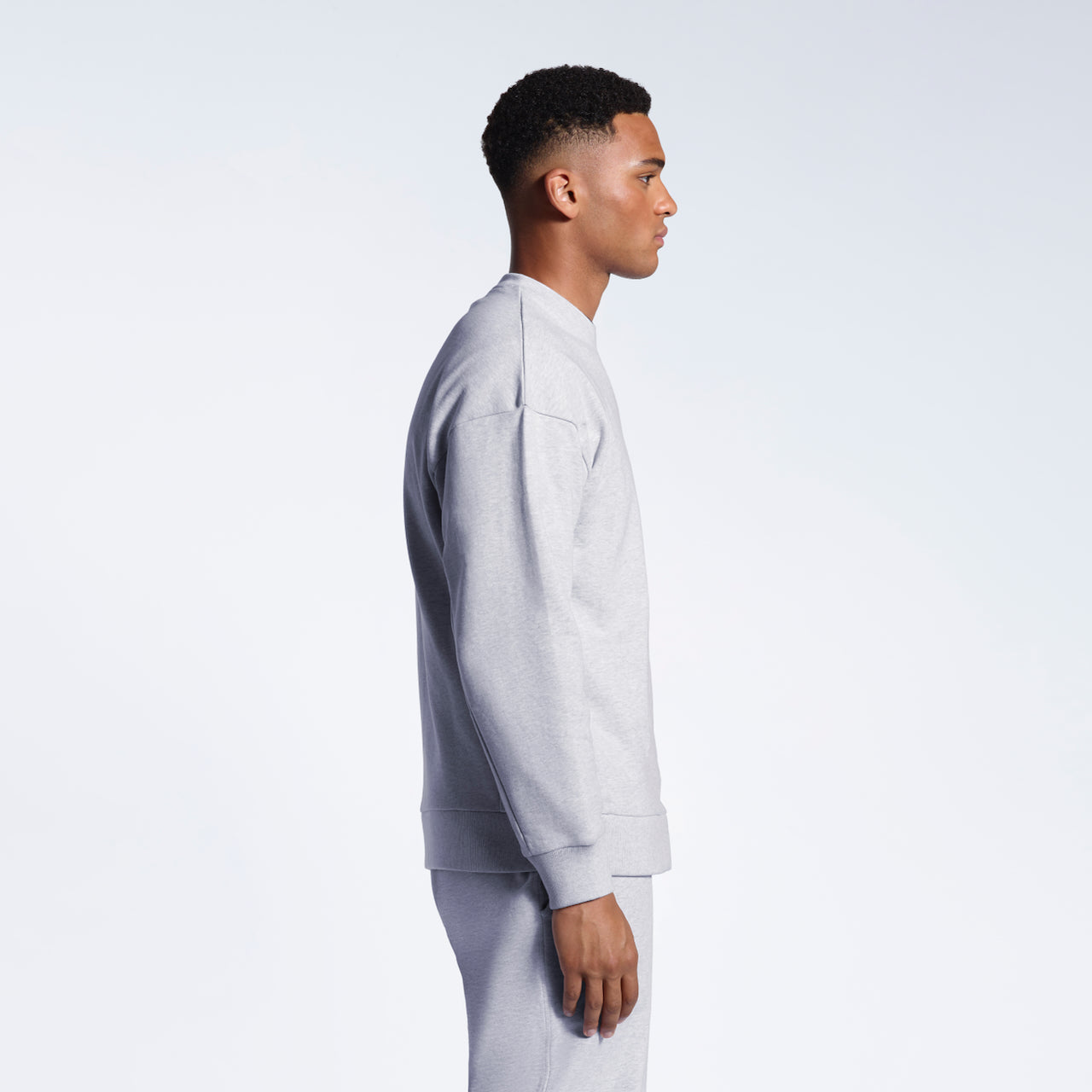 A man facing side on, modelling a grey oversized heavyweight organic cotton sweatshirt with matching joggers.
