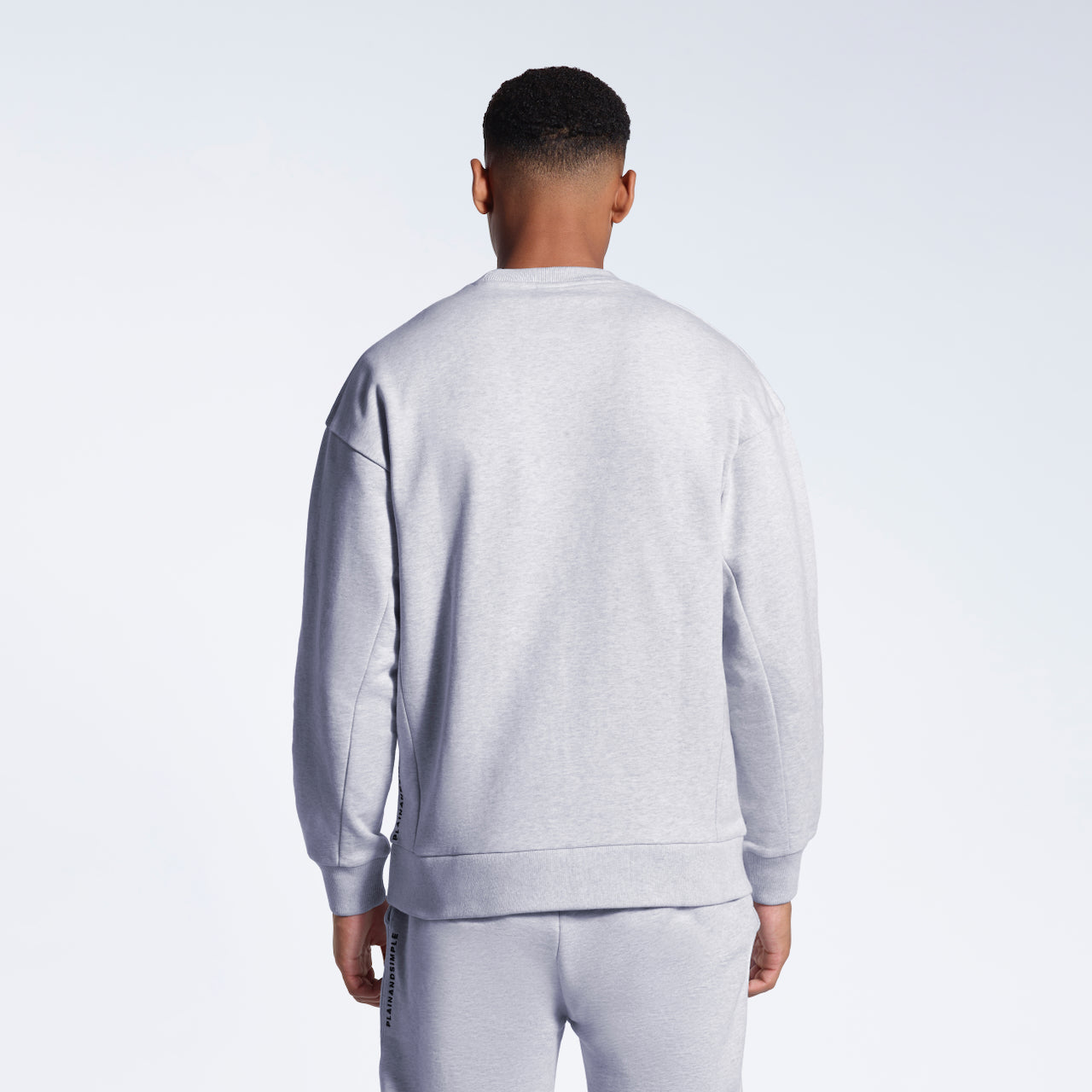A man facing away from the camera, showing the back of his grey oversized heavyweight organic cotton sweatshirt with matching joggers.