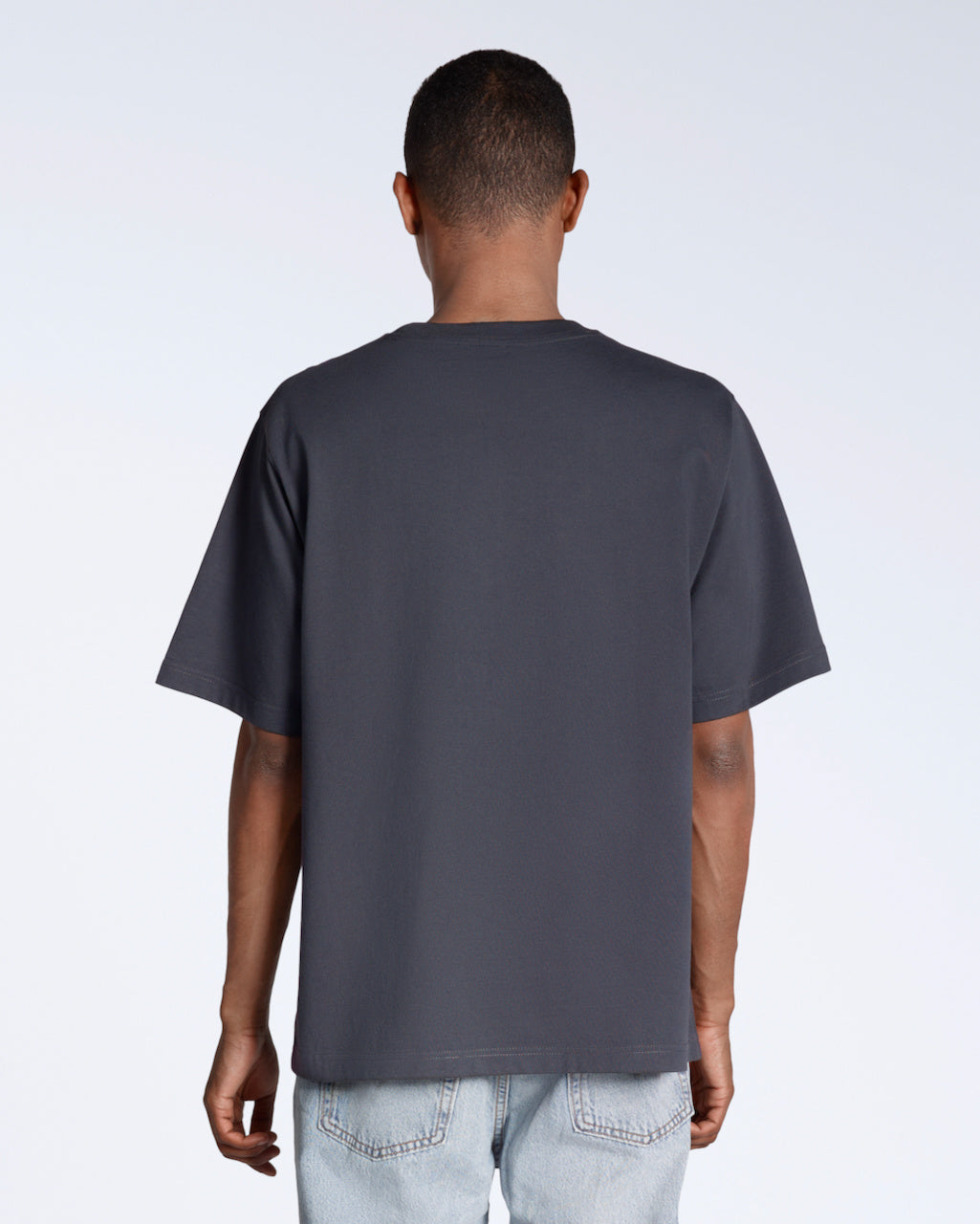 A man facing away from the camera, modelling a plain dark grey, oversized, organic cotton t shirt.