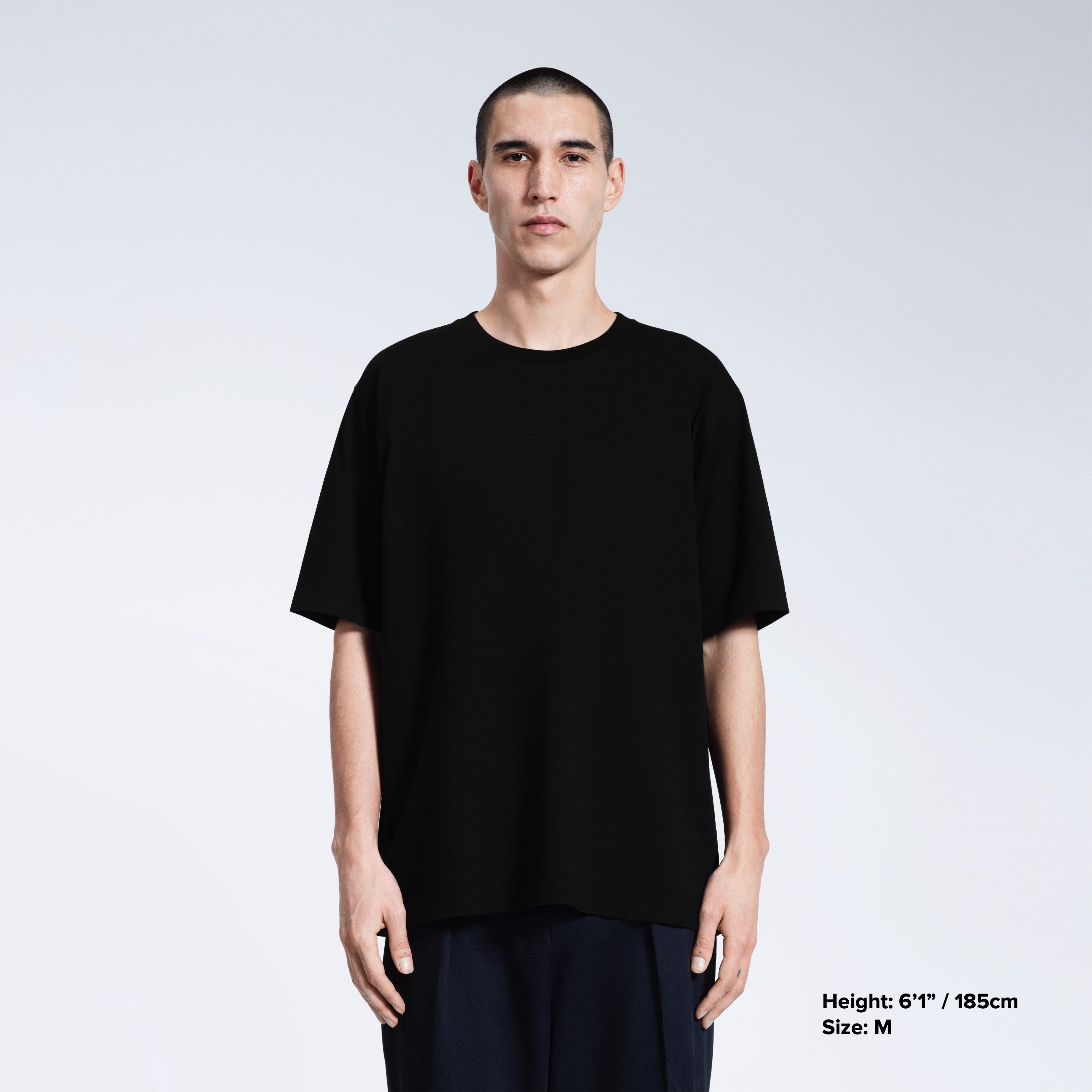 A man face on looking into the camera with his arms by his side, modelling a plain black oversized heavyweight organic cotton t shirt.