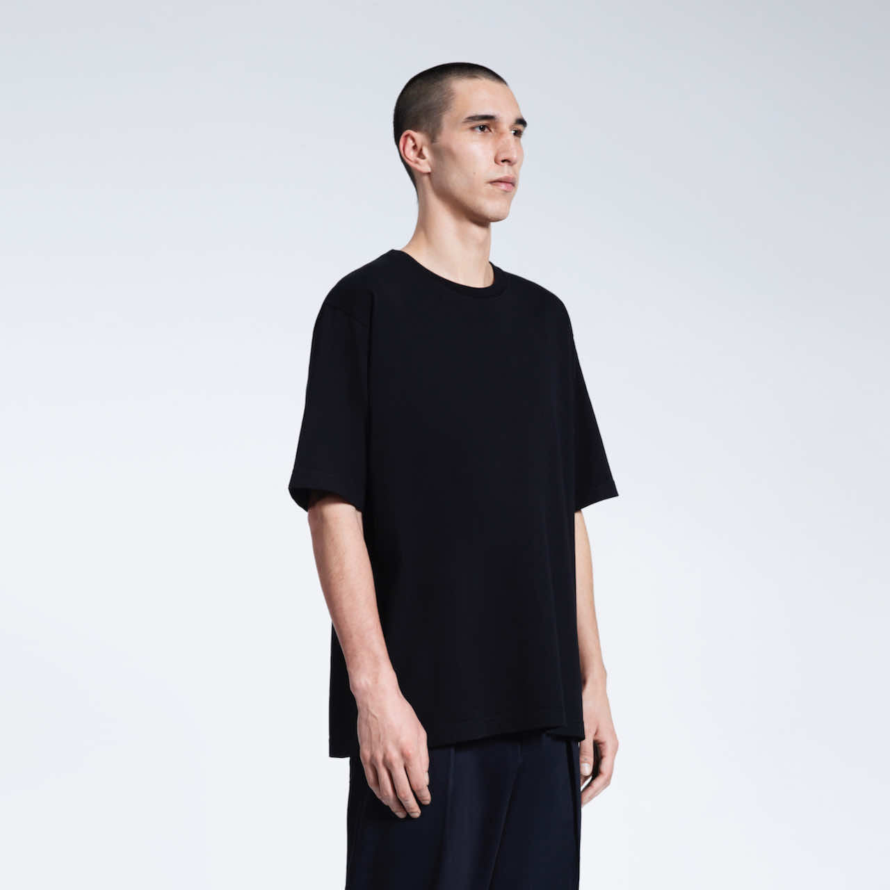 A man at an angle with his arms by his side, modelling a plain black oversized heavyweight organic cotton t shirt.