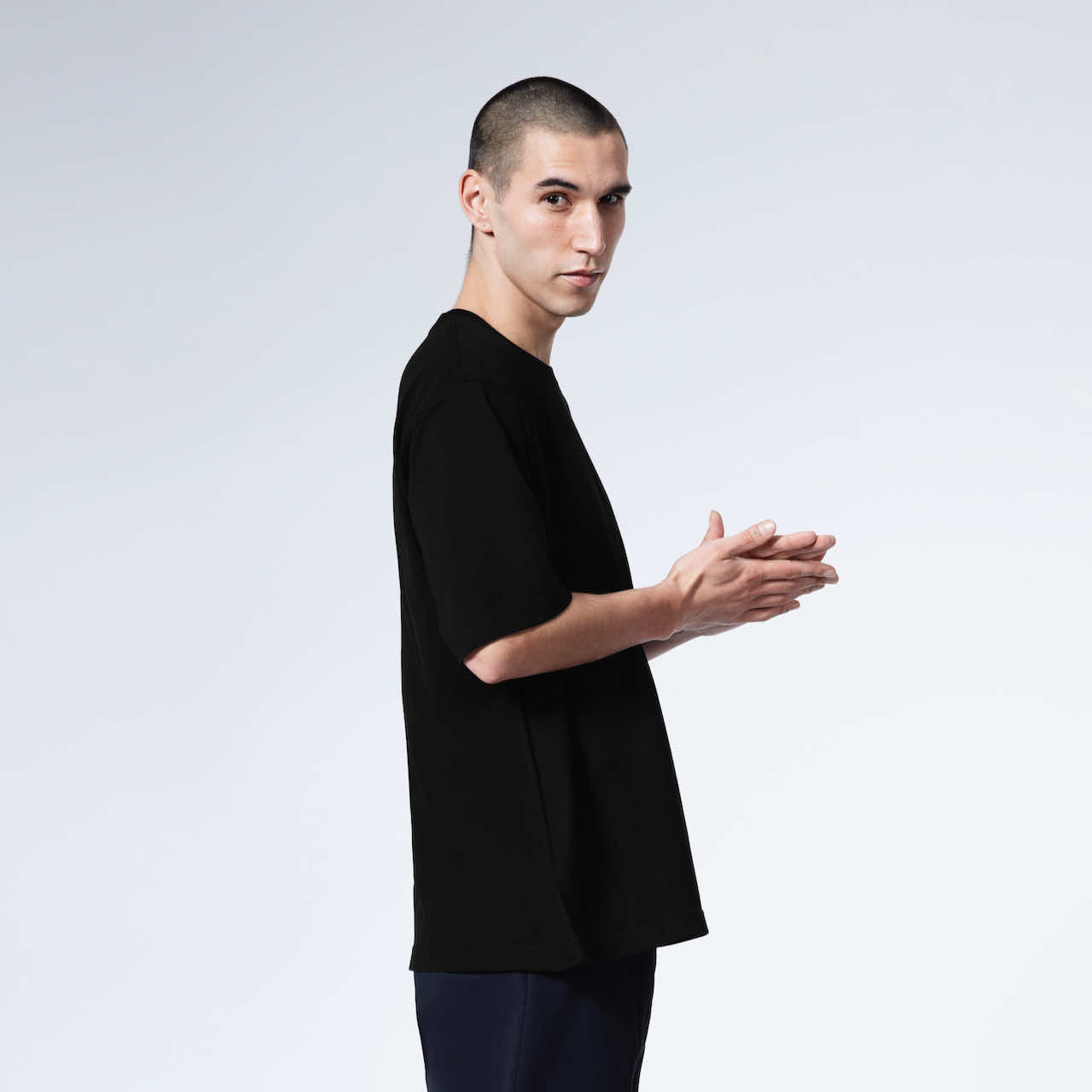 A man facing side on looking at the camera with his hands together, modelling a plain black oversized heavyweight organic cotton t shirt.