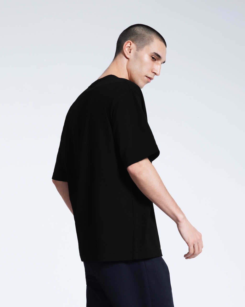 A man slightly turned towards the camera, modelling a plain black oversized heavyweight organic cotton t shirt.