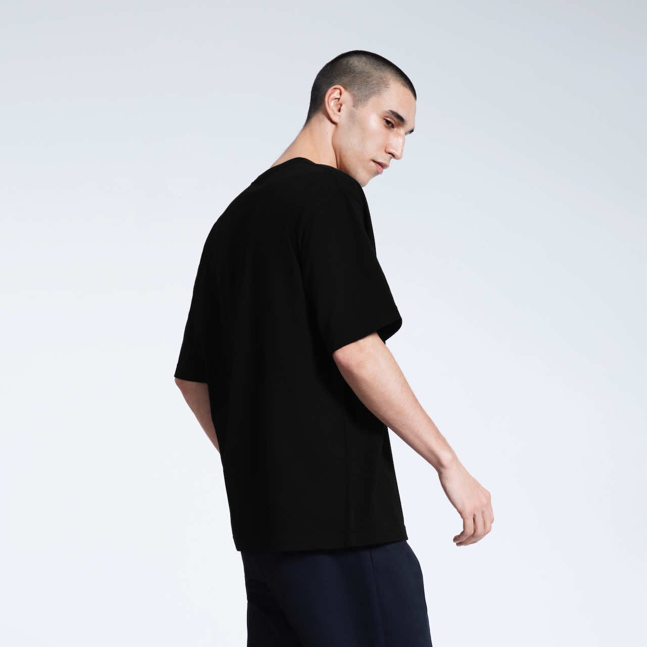 A man slightly turned towards the camera, modelling a plain black oversized heavyweight organic cotton t shirt.