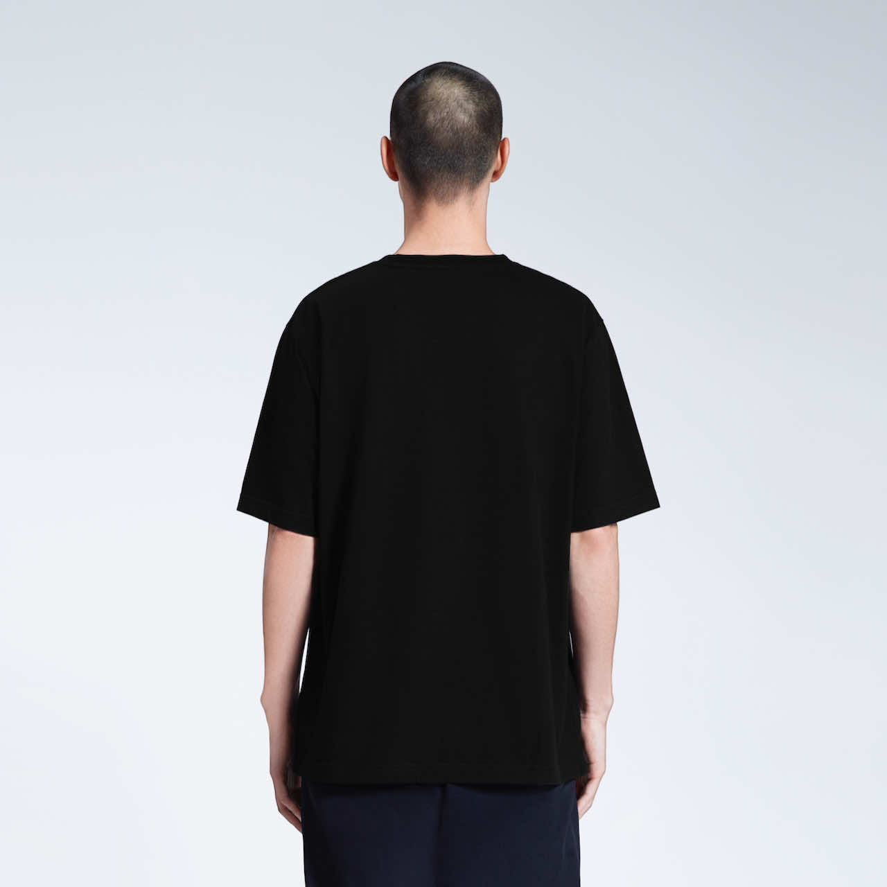 A man facing away from the camera with his arms by his side, modelling a plain black oversized heavyweight organic cotton t shirt.