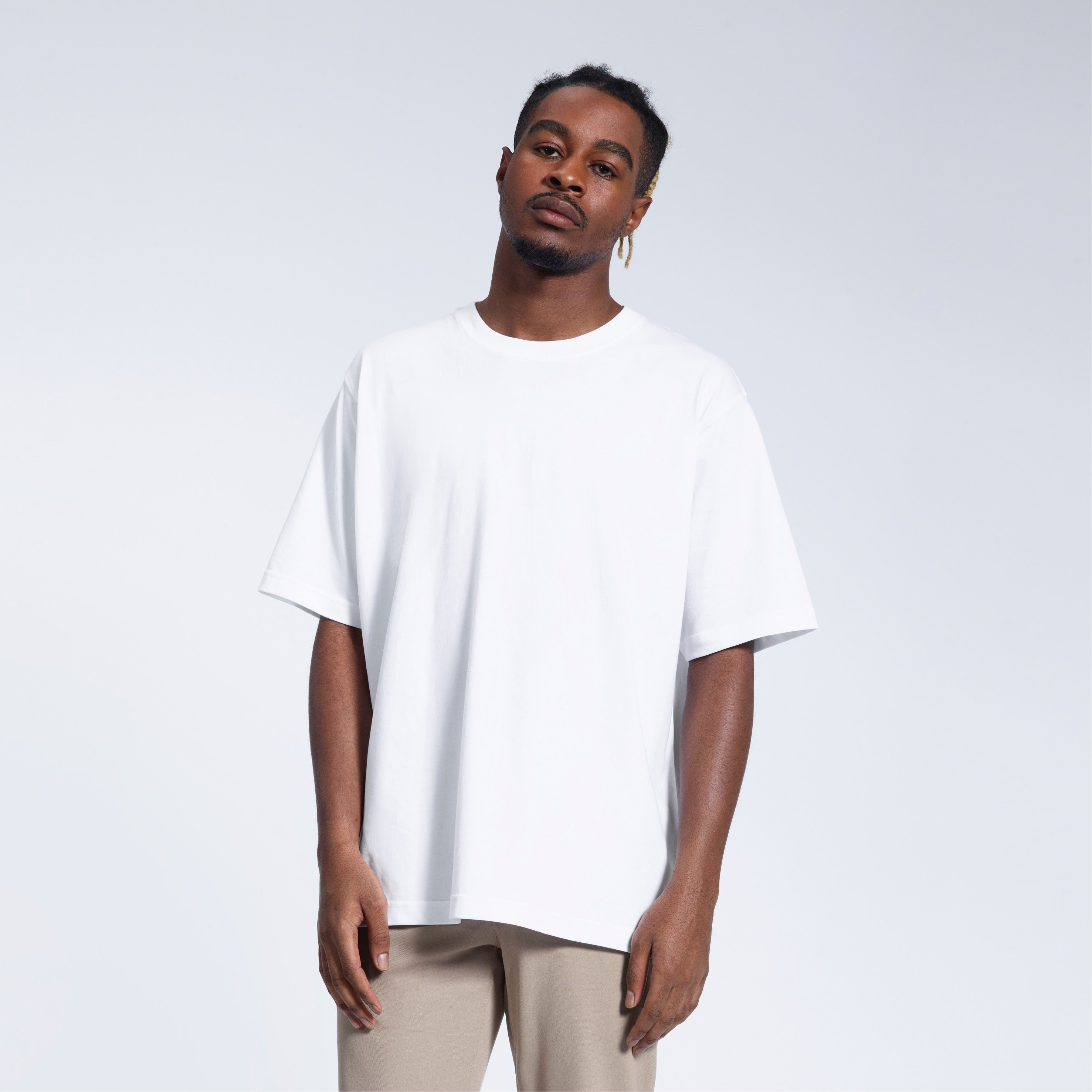 A man face on looking into the camera with his arms by his side, modelling a plain white oversized heavyweight organic cotton t shirt.