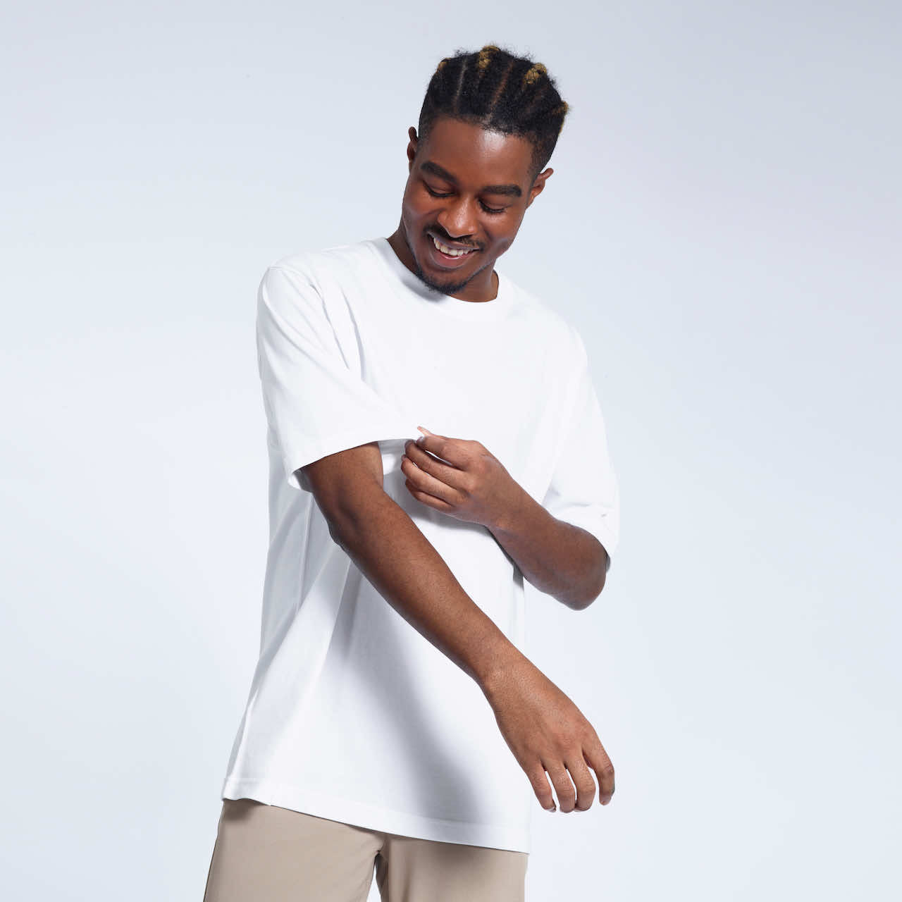 A man looking down and touching his sleeve, modelling a plain white oversized heavyweight organic cotton t shirt.