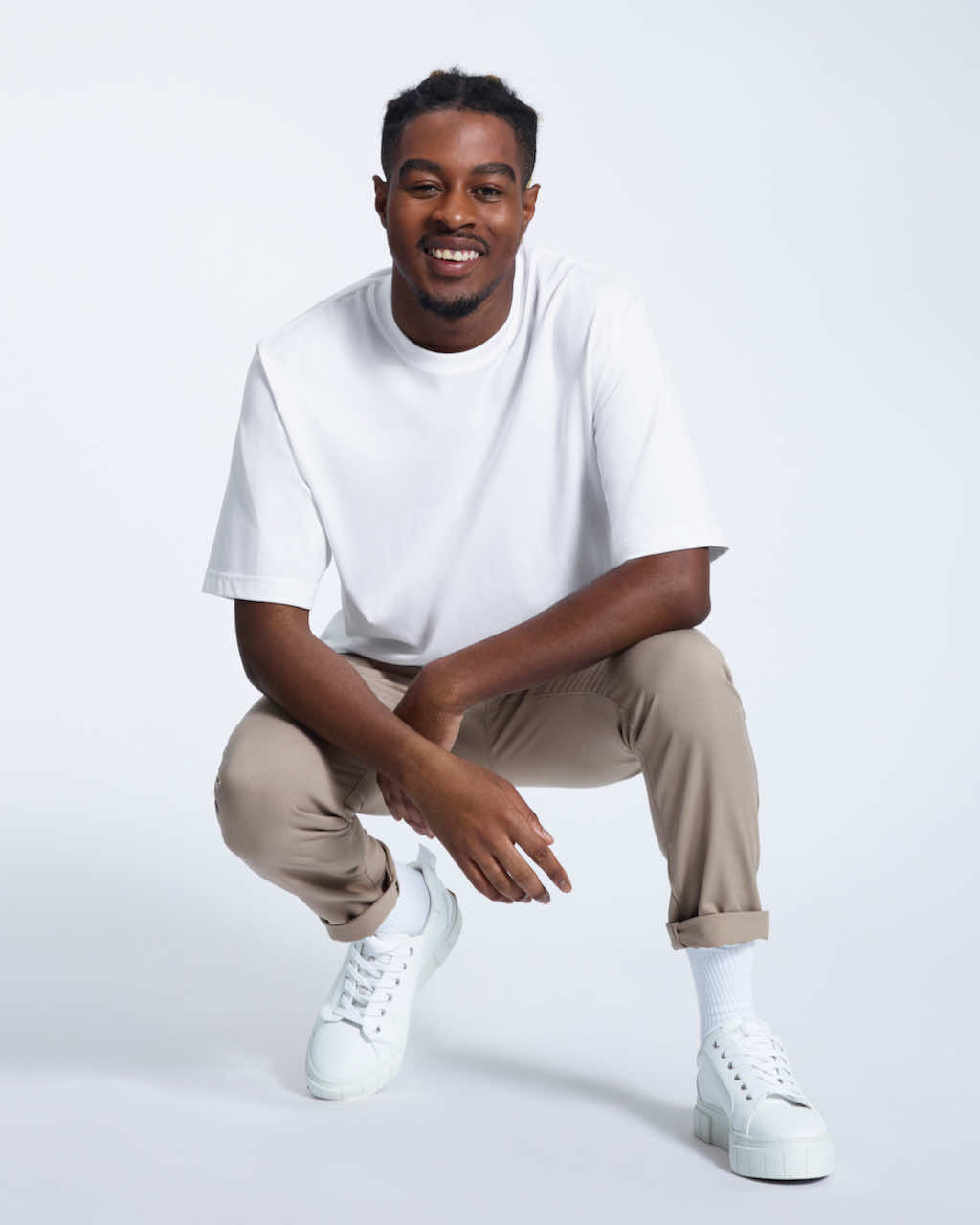 A man kneeling down smiling, modelling a plain white oversized heavyweight organic cotton t shirt.