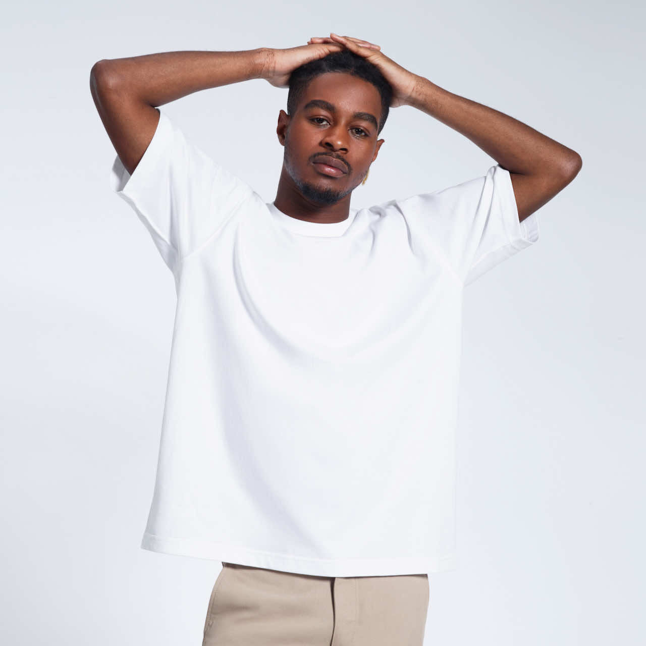A man looking into the camera with his hands on his head, modelling plain a white oversized heavyweight organic cotton t shirt.