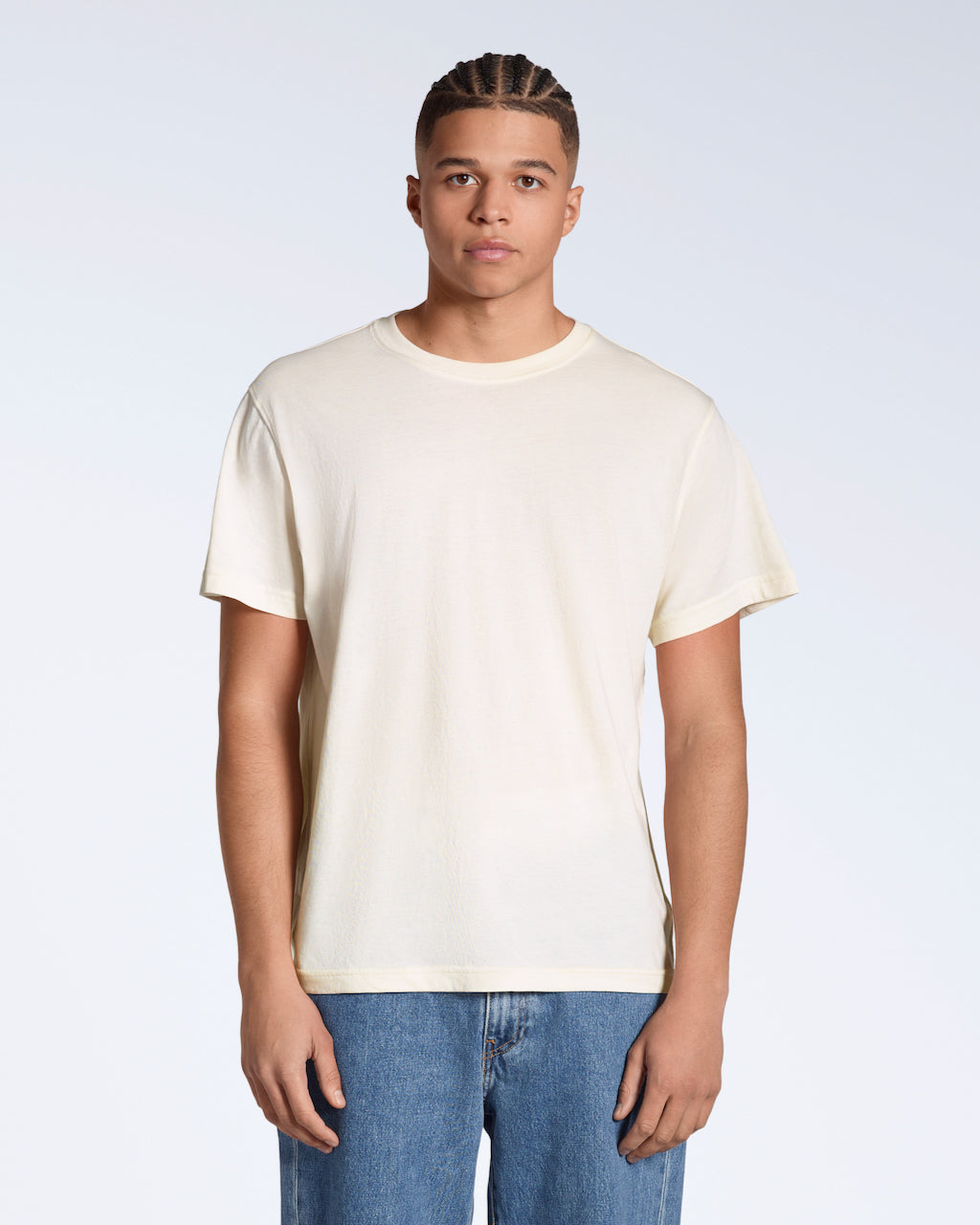 A man facing front on looking into the camera, modelling a plain natural coloured, organic cotton t shirt.