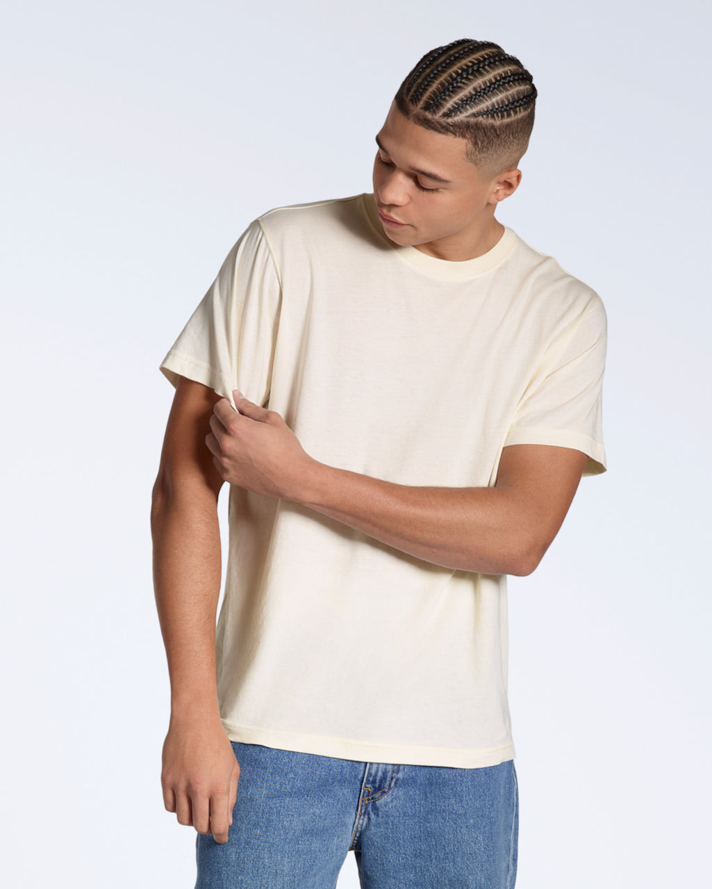 A man looking down touching his sleeve,, modelling a plain, natural coloured, organic cotton t shirt.