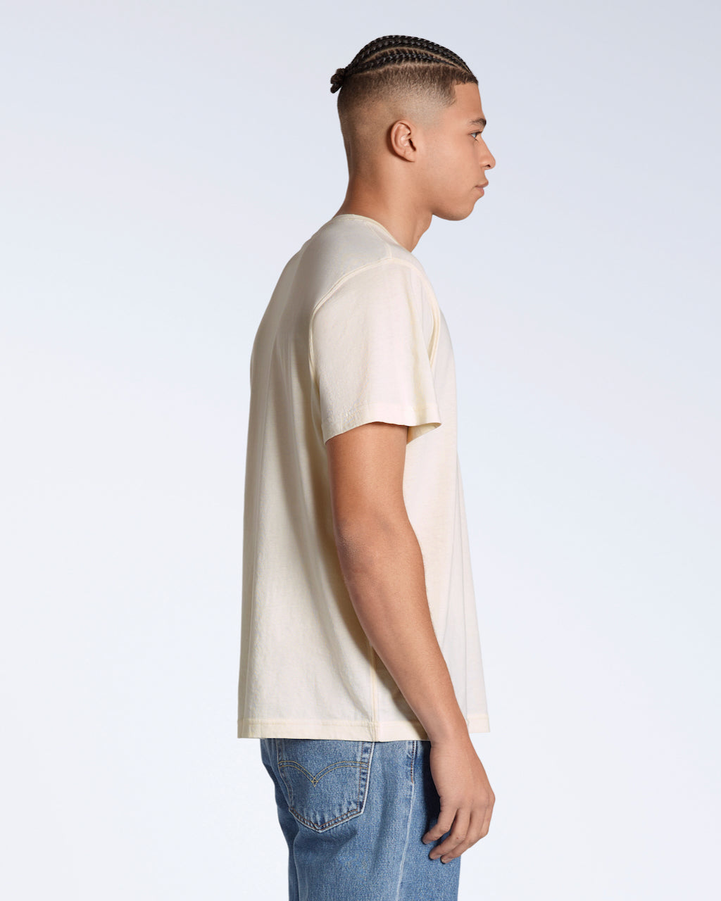 A man facing side on, modelling a plain, natural coloured, short sleeve organic cotton t shirt.