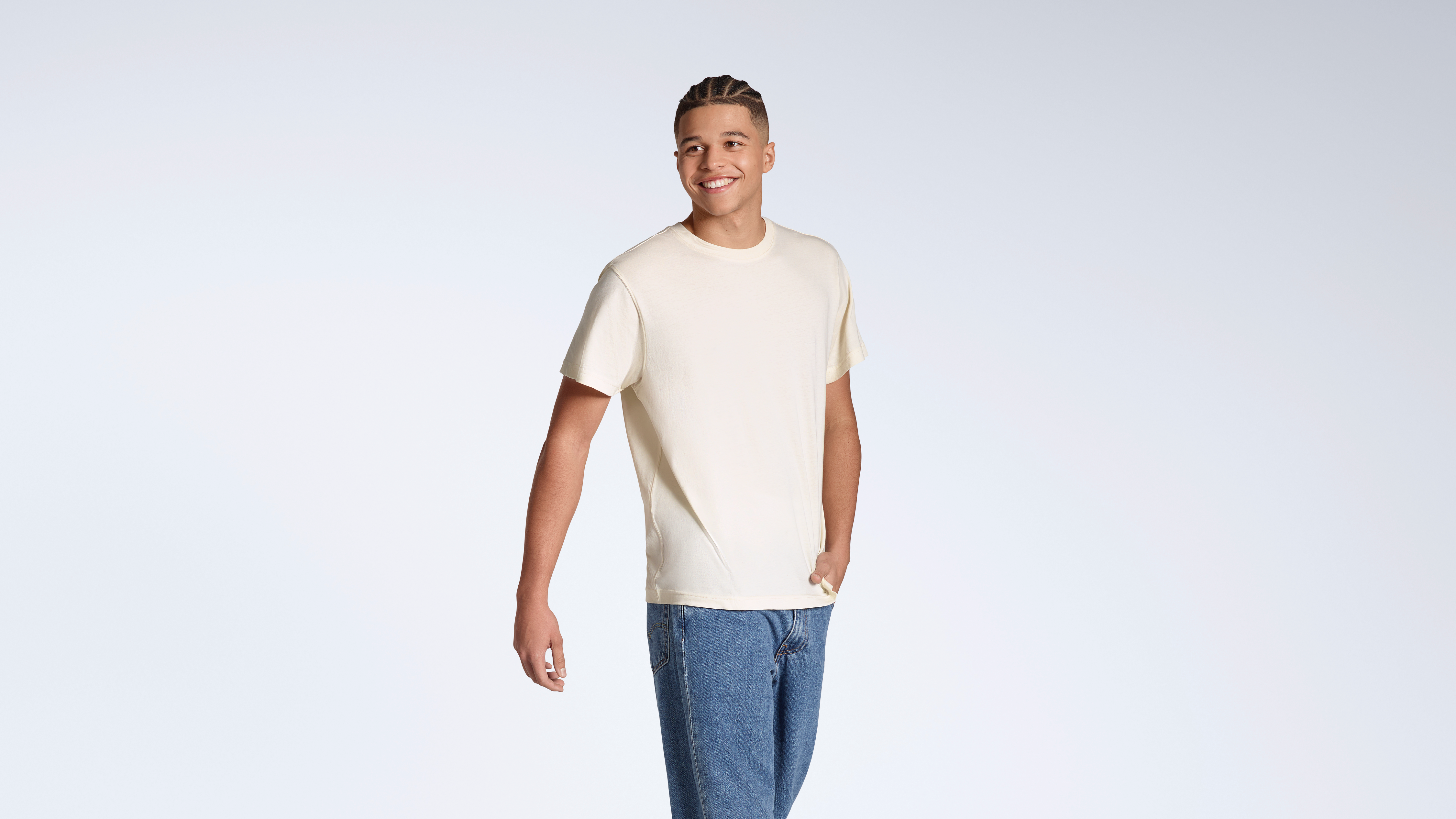 A man smiling with his hand in his pocket, modelling a plain, natural coloured, organic cotton t shirt.
