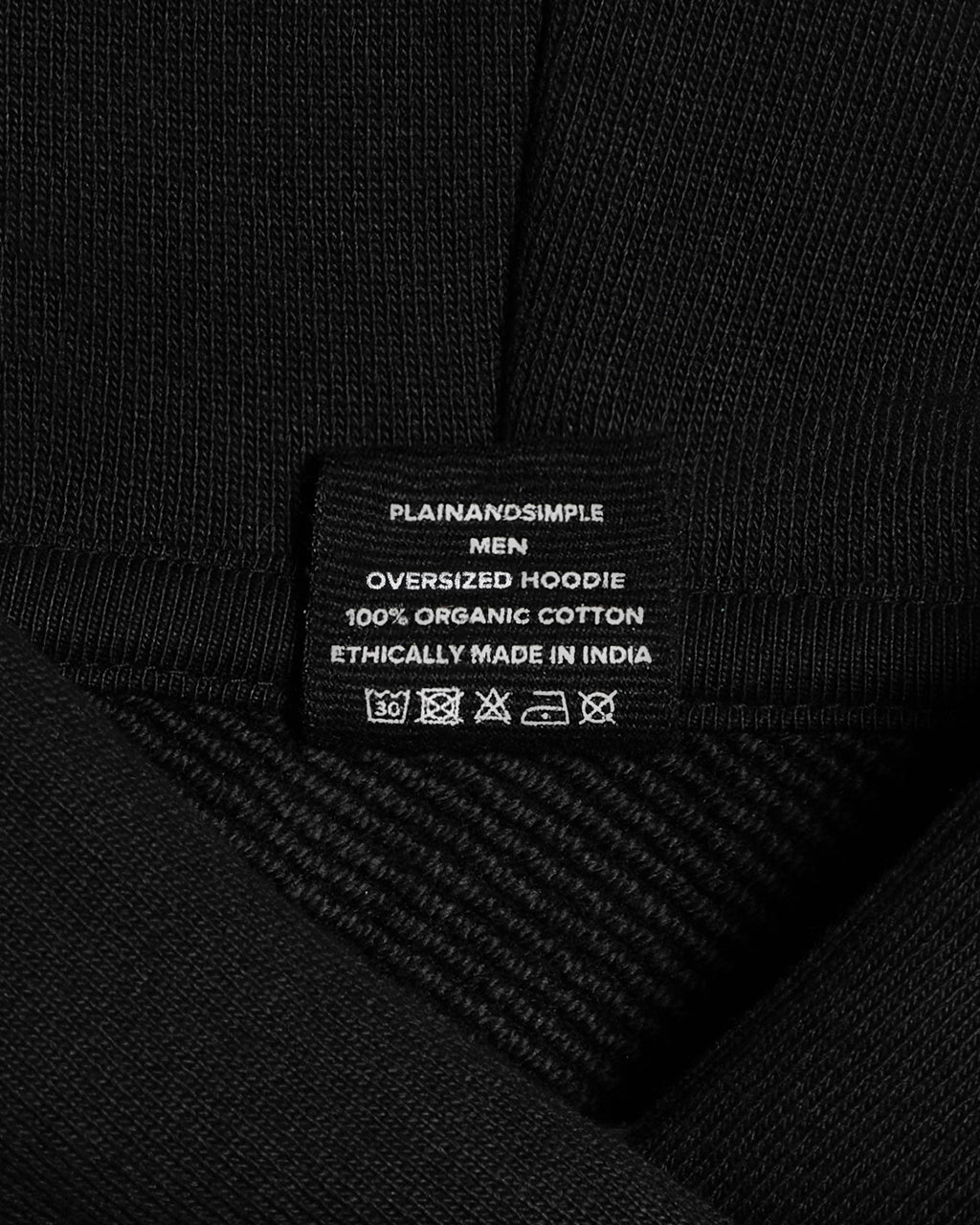 A close up of a neck label in a men's black, oversized, organic cotton hoodie.