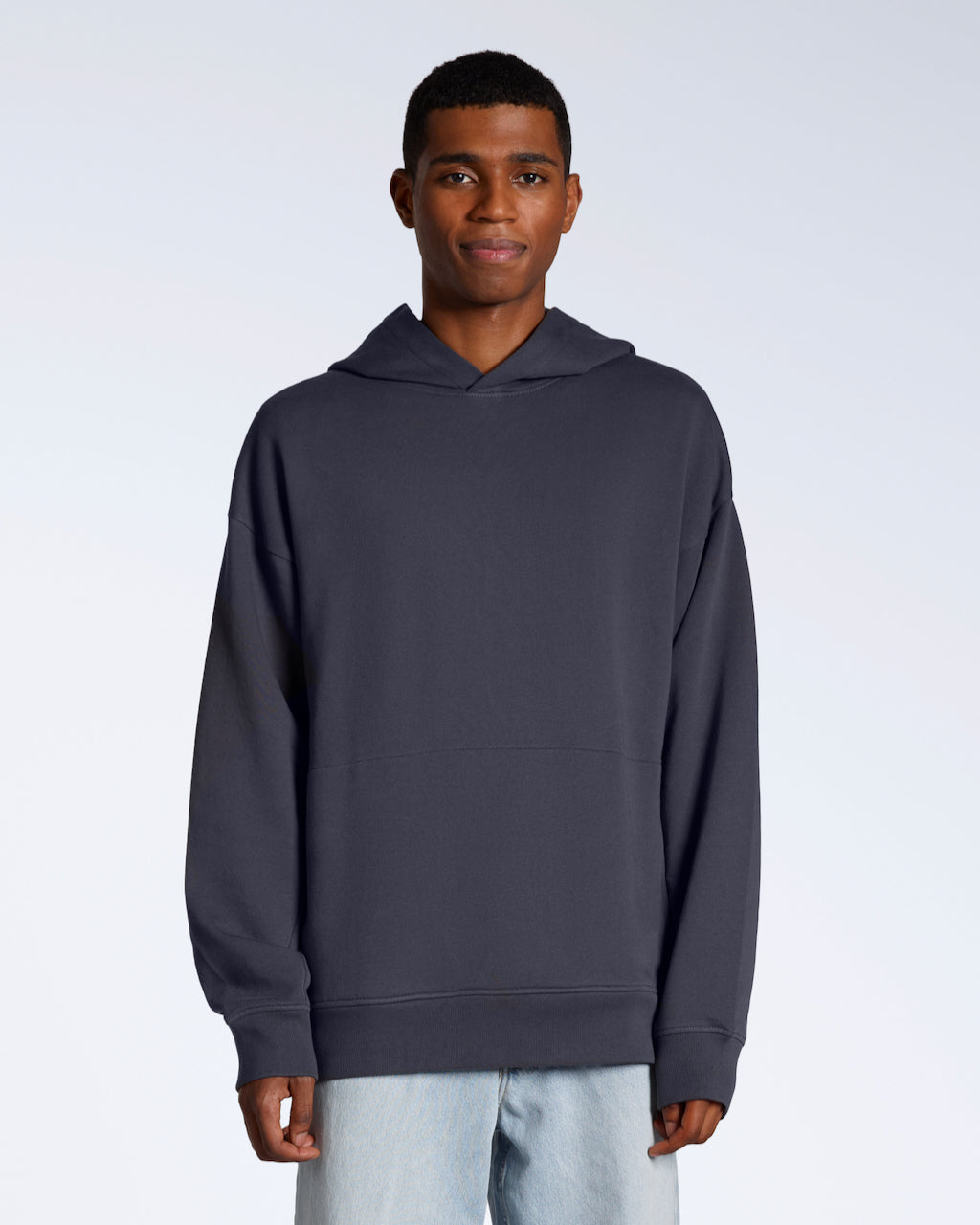A man facing front on looking into the camera with his arms by his sides, modelling a dark grey oversized organic cotton hoodie.
