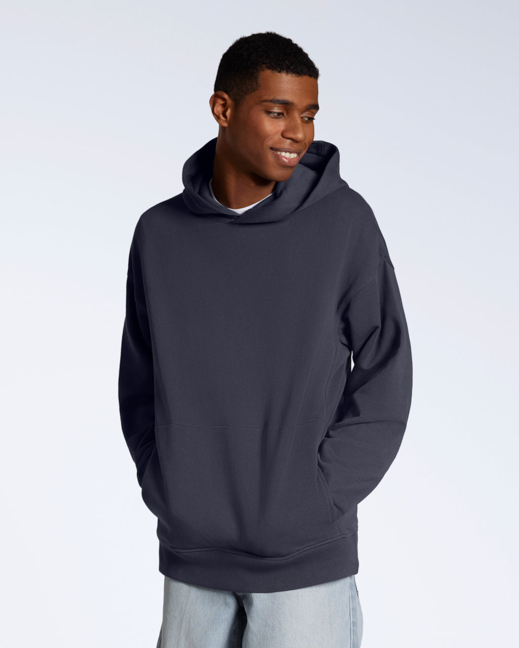 A man smiling with his hands in his pockets, modelling a dark grey oversized organic cotton hoodie.