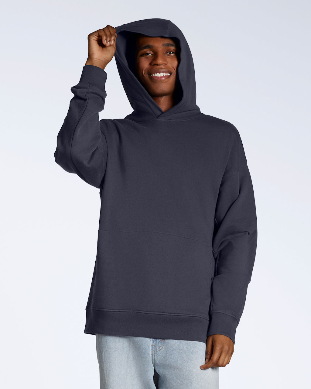 A man smiling into the camera whilst touching his hood, modelling a dark grey oversized organic cotton hoodie.