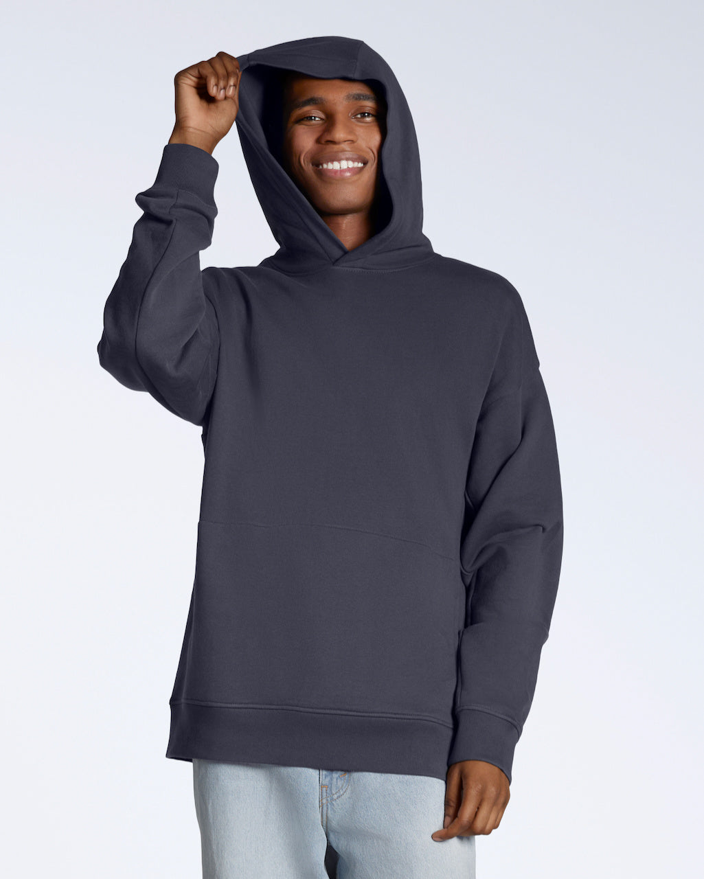 A man smiling into the camera whilst touching his hood, modelling a dark grey oversized organic cotton hoodie.