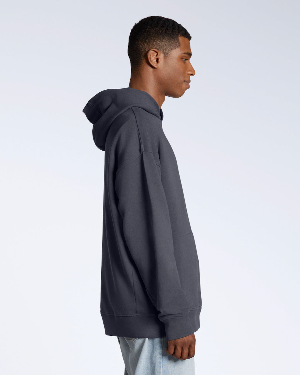 A man facing side on, modelling a dark grey oversized organic cotton hoodie.