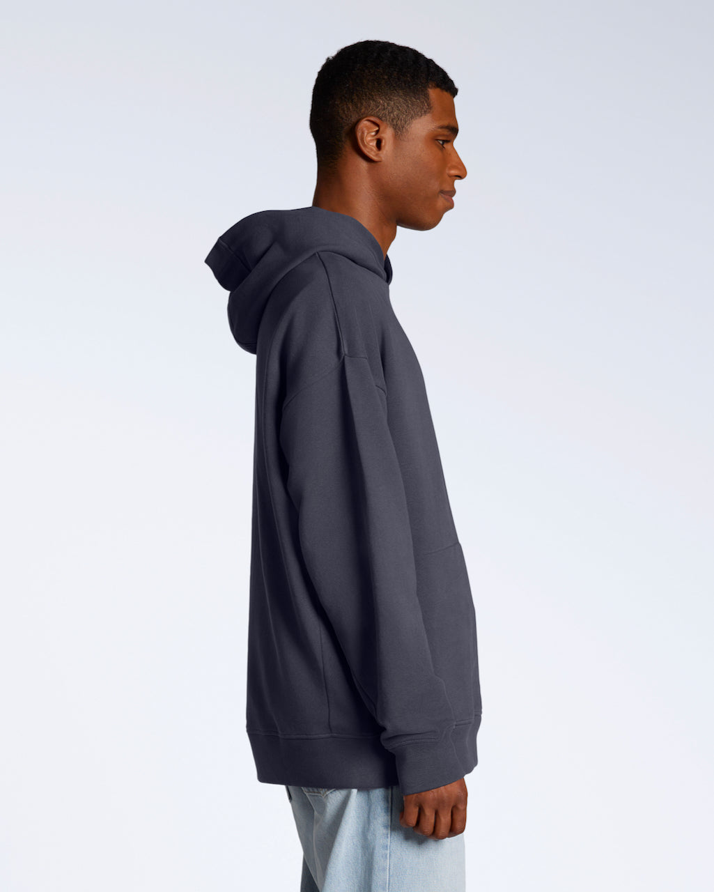 A man facing side on, modelling a dark grey oversized organic cotton hoodie.