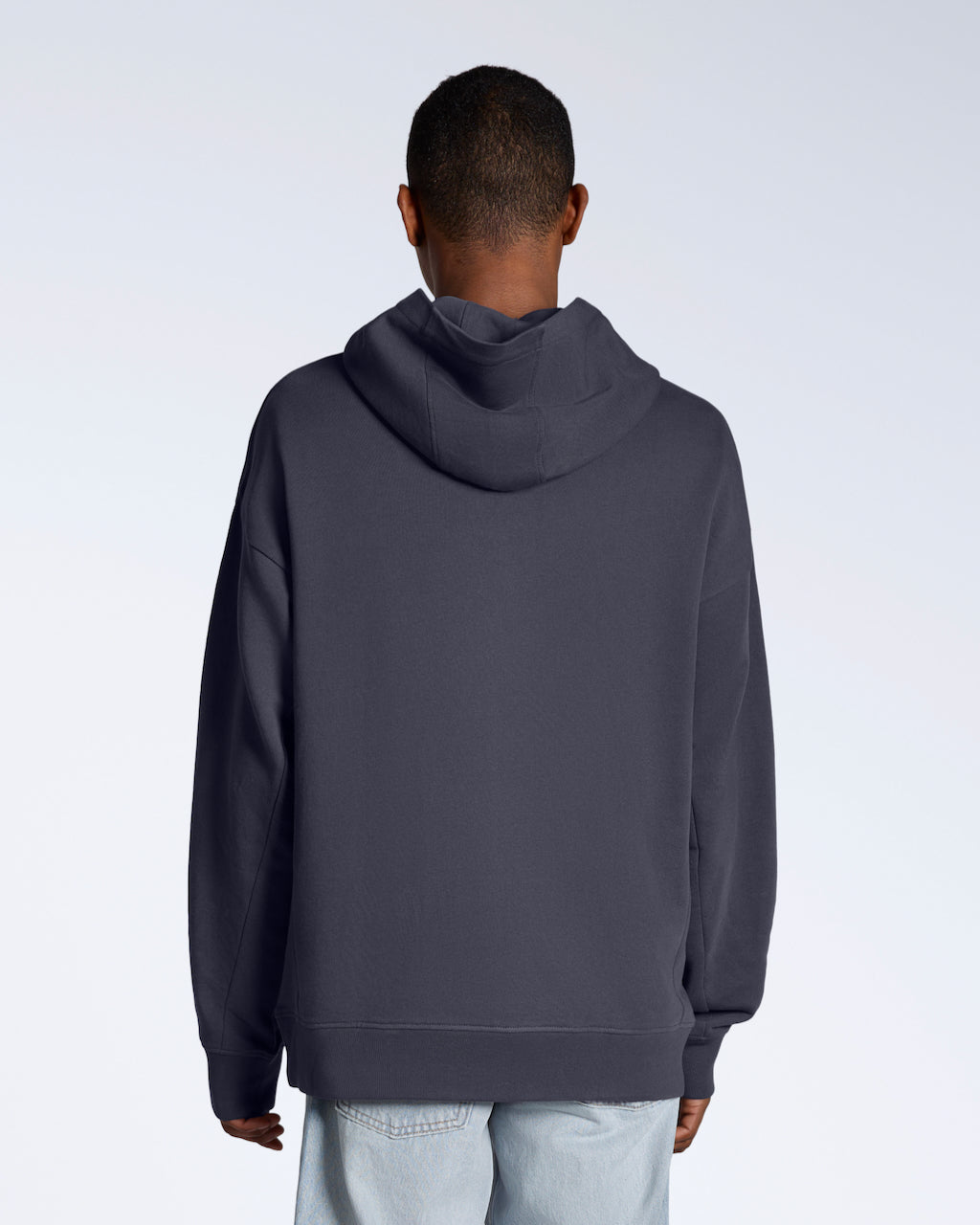 A man facing away from the camera with his arms by his sides, modelling a dark grey oversized organic cotton hoodie.